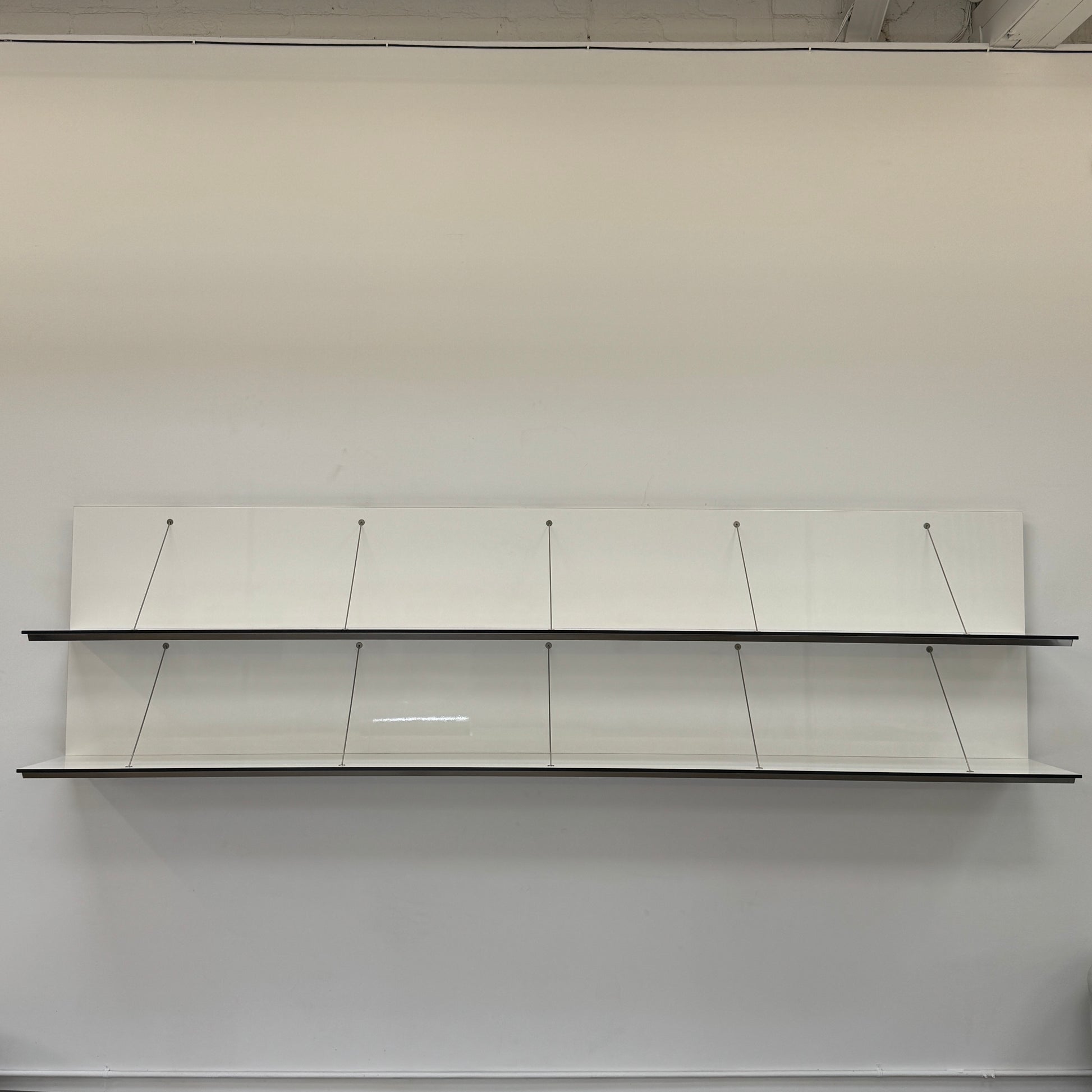 Two long, empty black shelves from the B&B Italia PAB Shelving collection are mounted on a white wall, supported by evenly spaced metal brackets.