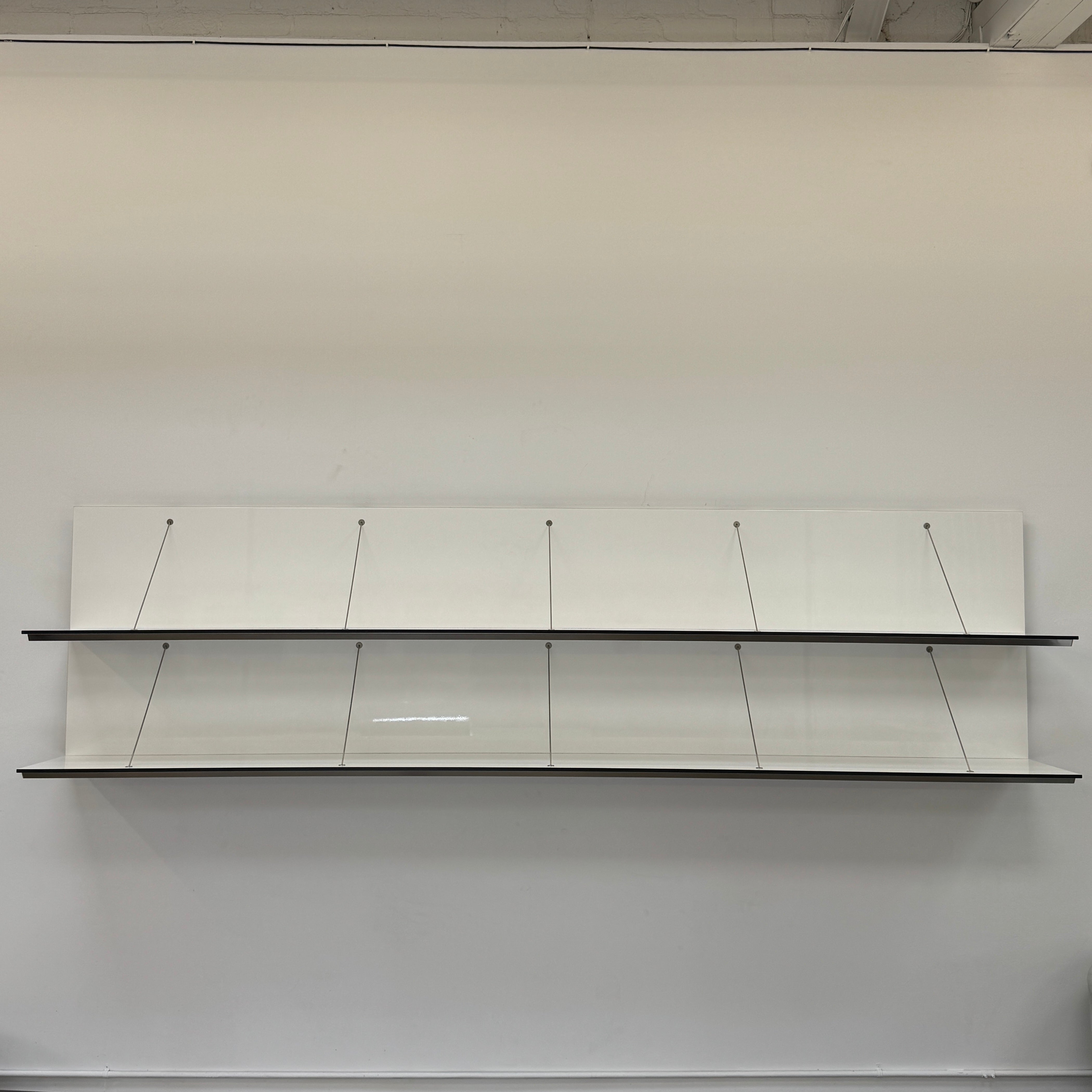Two long, empty black shelves from the B&B Italia PAB Shelving collection are mounted on a white wall, supported by evenly spaced metal brackets.