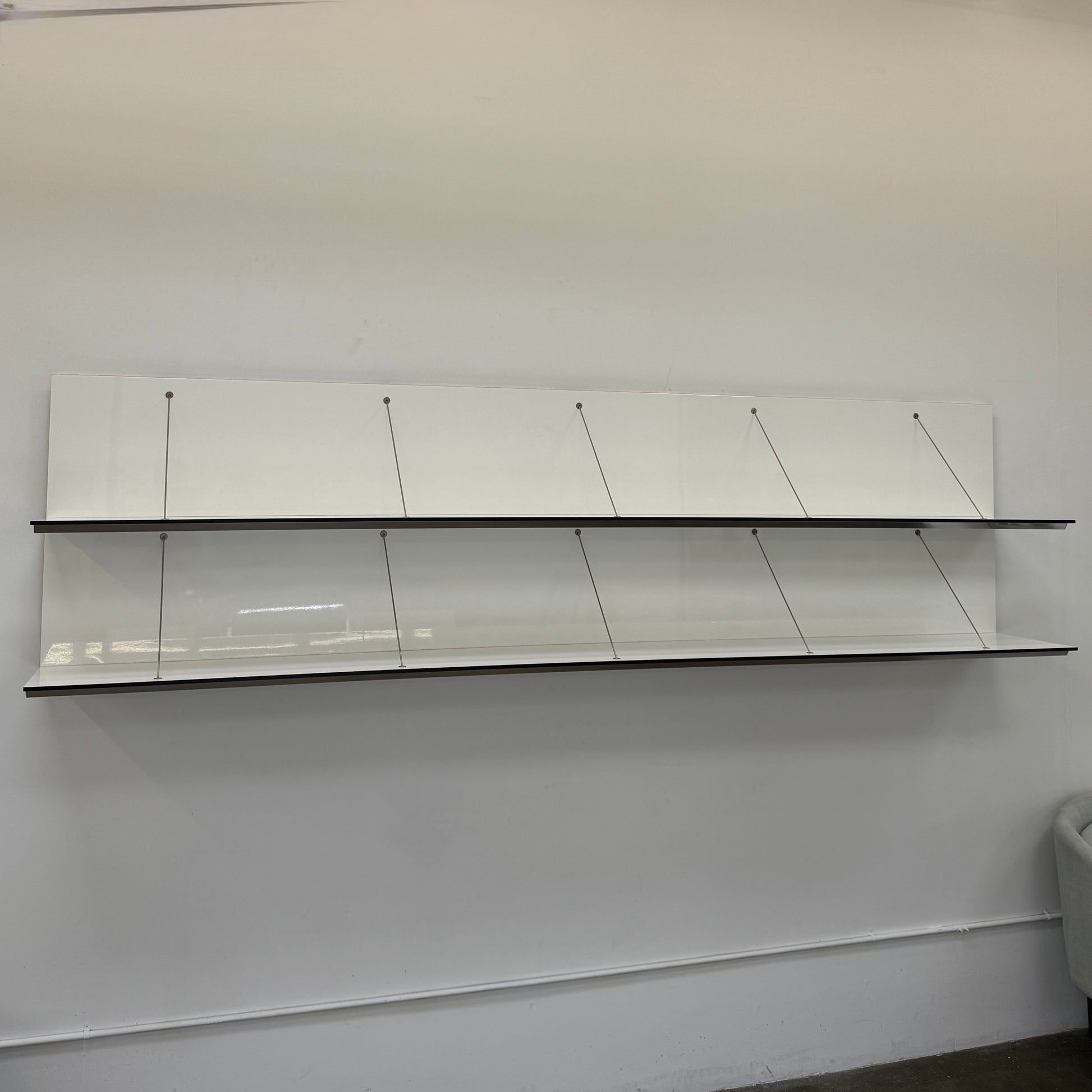 Two long, empty black shelves from the B&B Italia PAB Shelving collection are mounted on a white wall, supported by evenly spaced metal brackets.