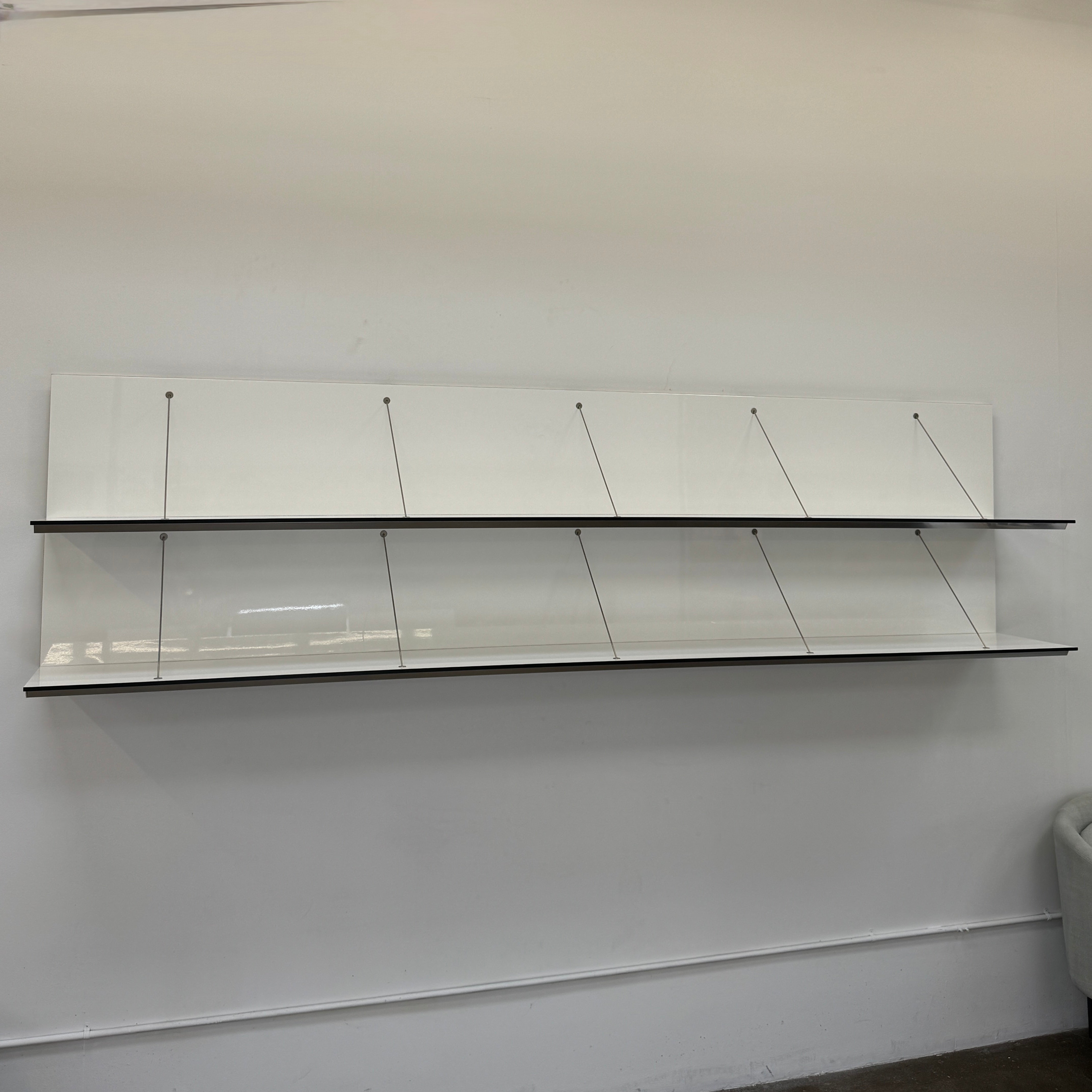 Two long, empty black shelves from the B&B Italia PAB Shelving collection are mounted on a white wall, supported by evenly spaced metal brackets.
