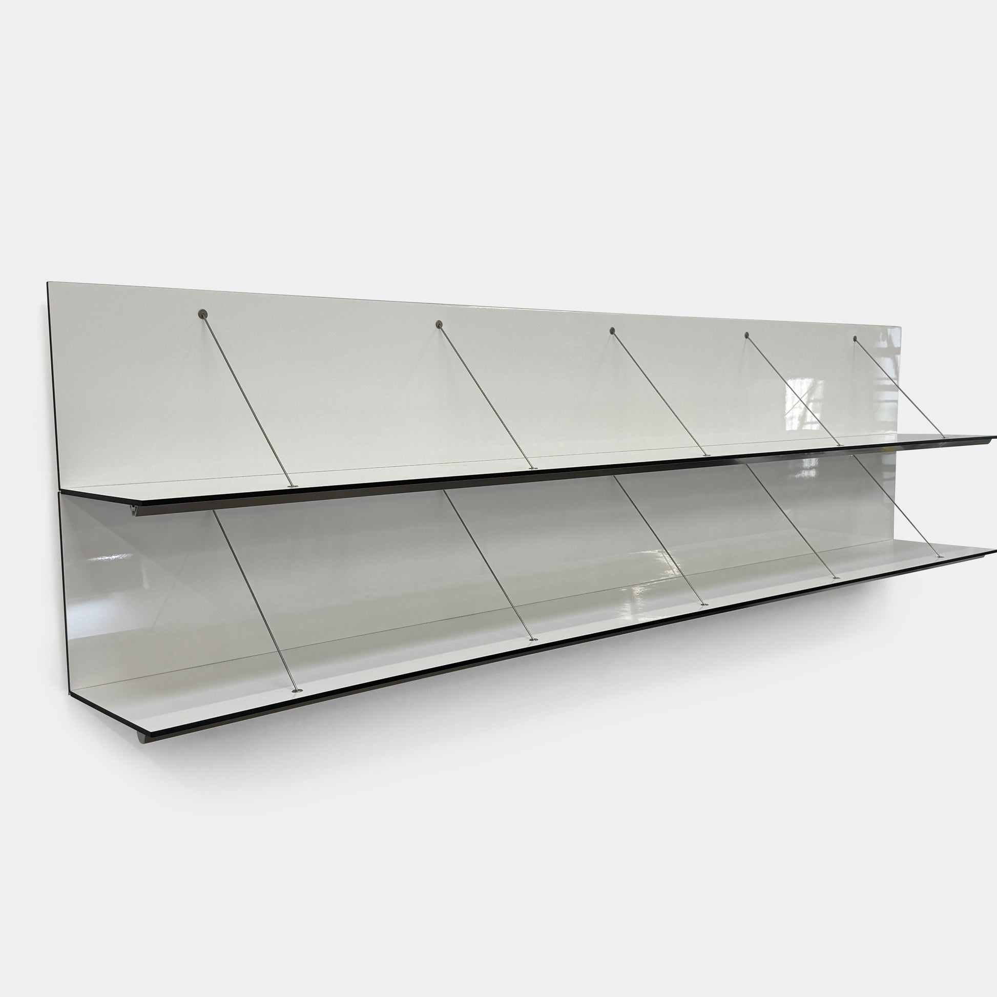 Two long, empty black shelves from the B&B Italia PAB Shelving collection are mounted on a white wall, supported by evenly spaced metal brackets.
