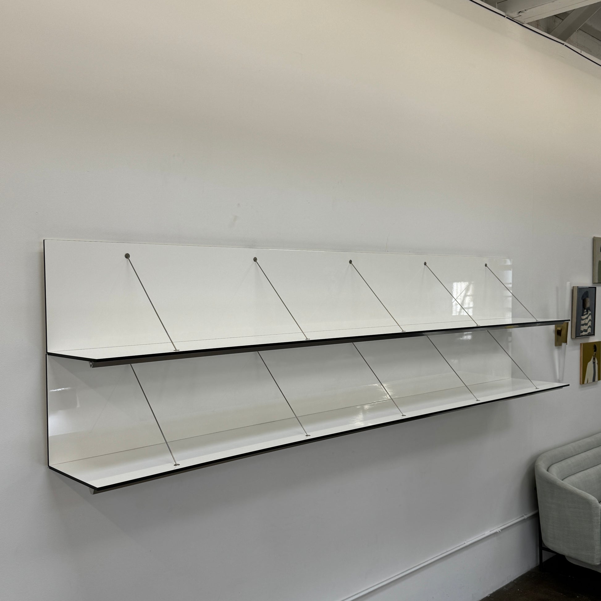 Two long, empty black shelves from the B&B Italia PAB Shelving collection are mounted on a white wall, supported by evenly spaced metal brackets.