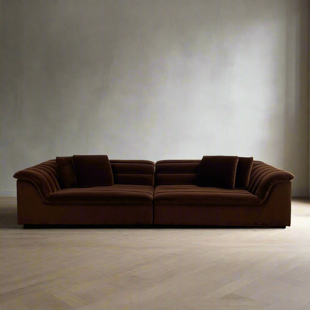 The Ellison Studios Float Sofa is a dark brown sectional from Ellison Studios with velvet upholstery, low profile, channel tufting, and two large cushions for extra comfort.