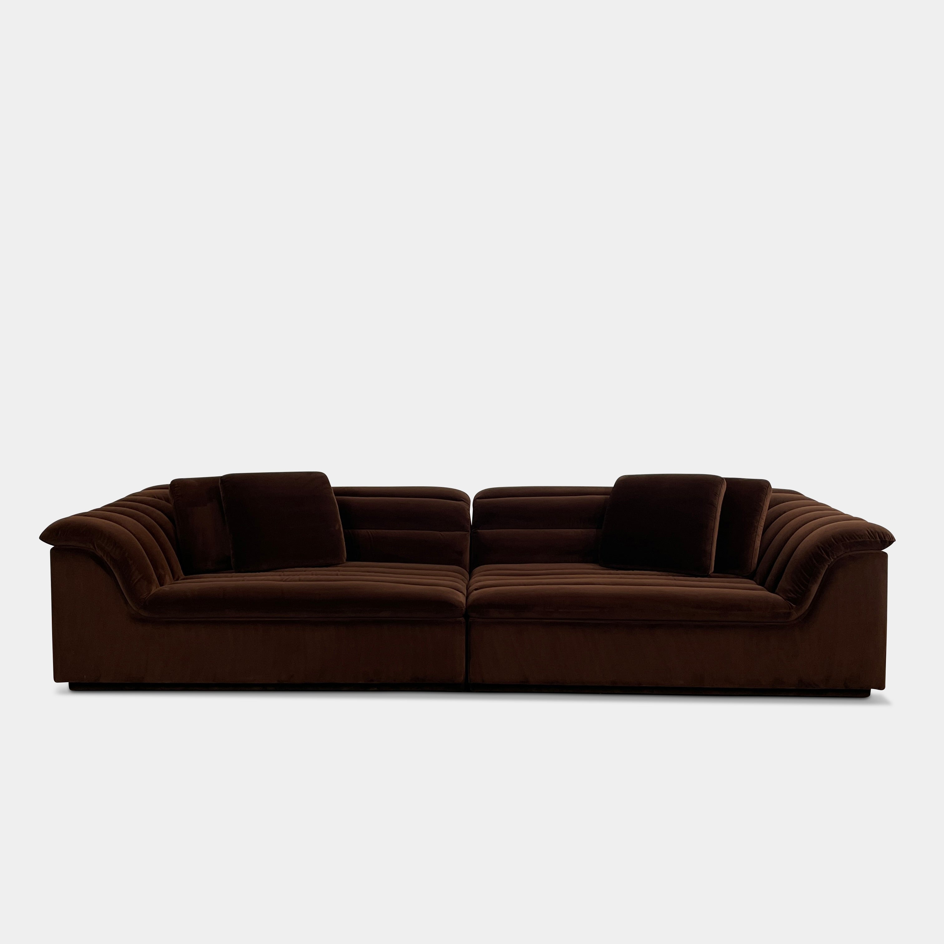 The Ellison Studios Float Sofa is a dark brown sectional from Ellison Studios with velvet upholstery, low profile, channel tufting, and two large cushions for extra comfort.