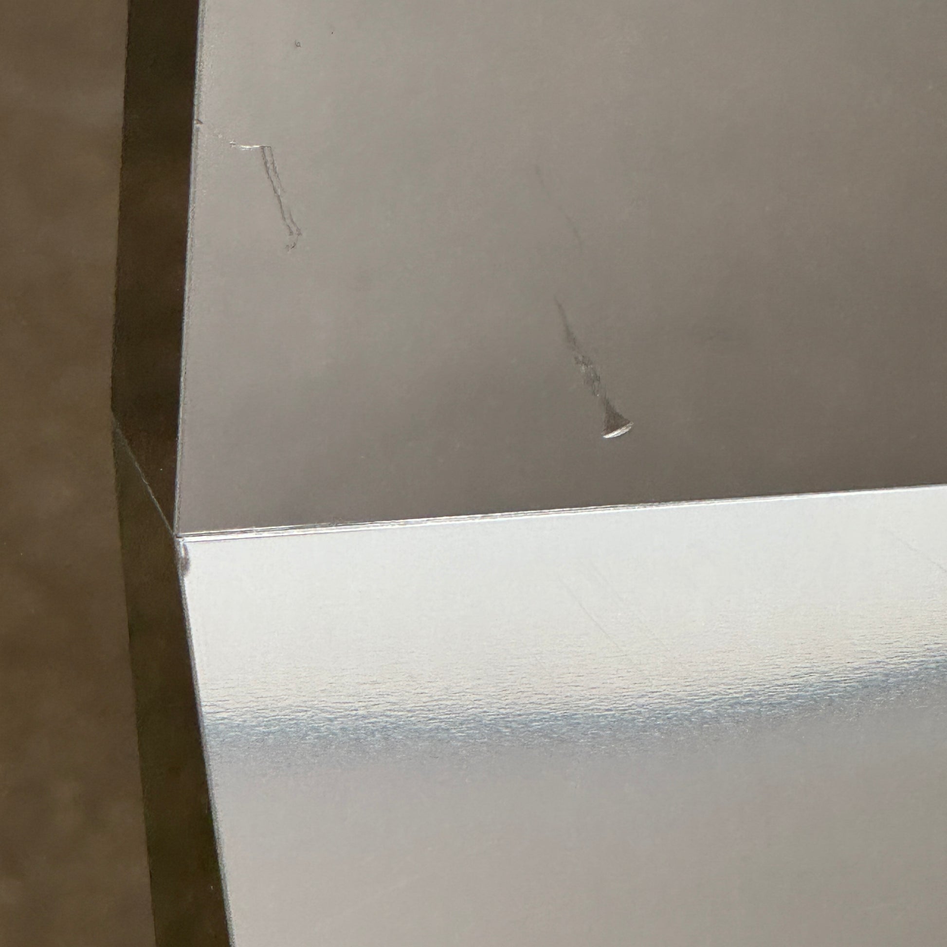 The Molteni & C Diamond table features a rectangular black marble top and angled polished metal legs, set on a brown concrete floor against a plain white wall. This piece by Molteni & C adds sophisticated elegance to any space.