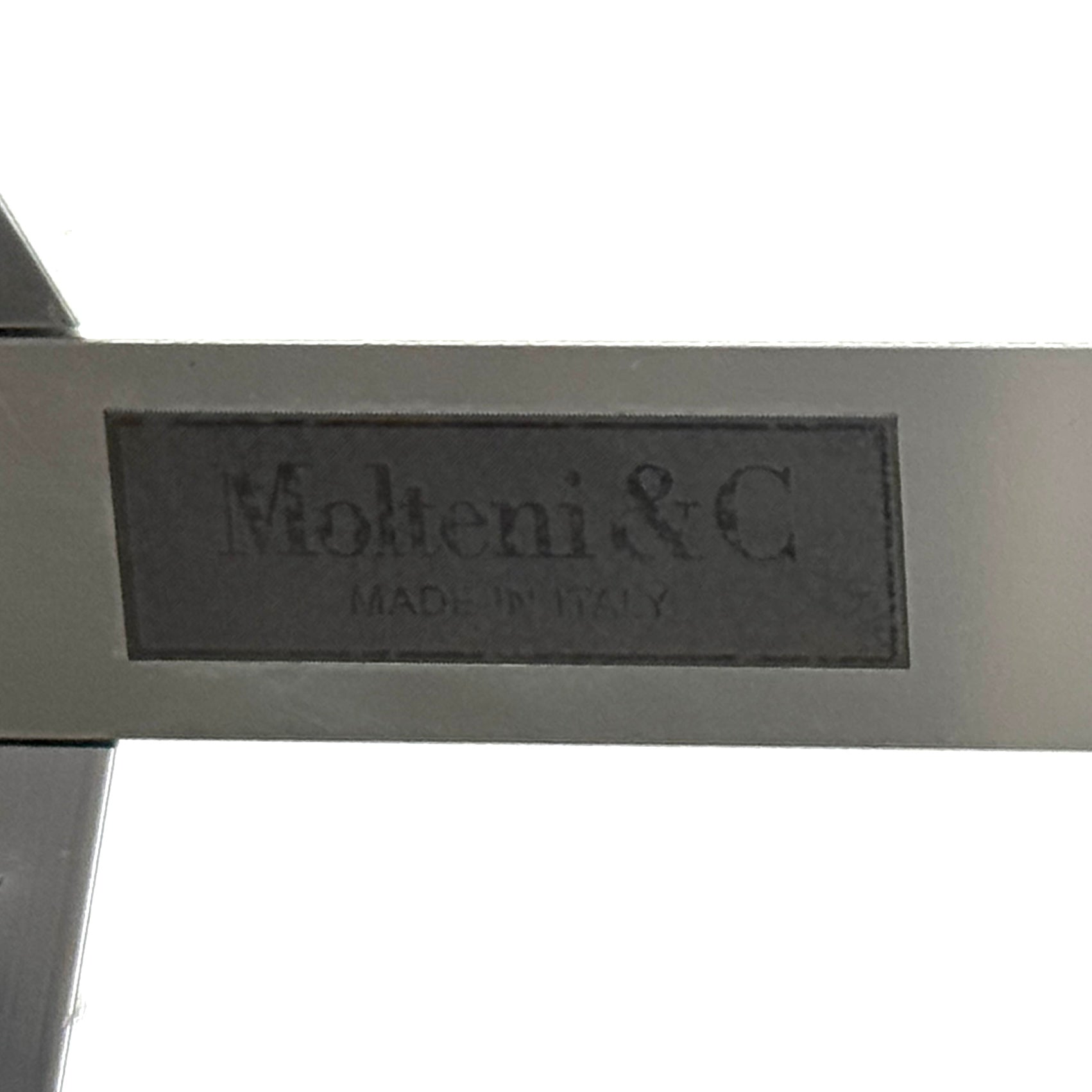 The Molteni & C Diamond table features a rectangular black marble top and angled polished metal legs, set on a brown concrete floor against a plain white wall. This piece by Molteni & C adds sophisticated elegance to any space.