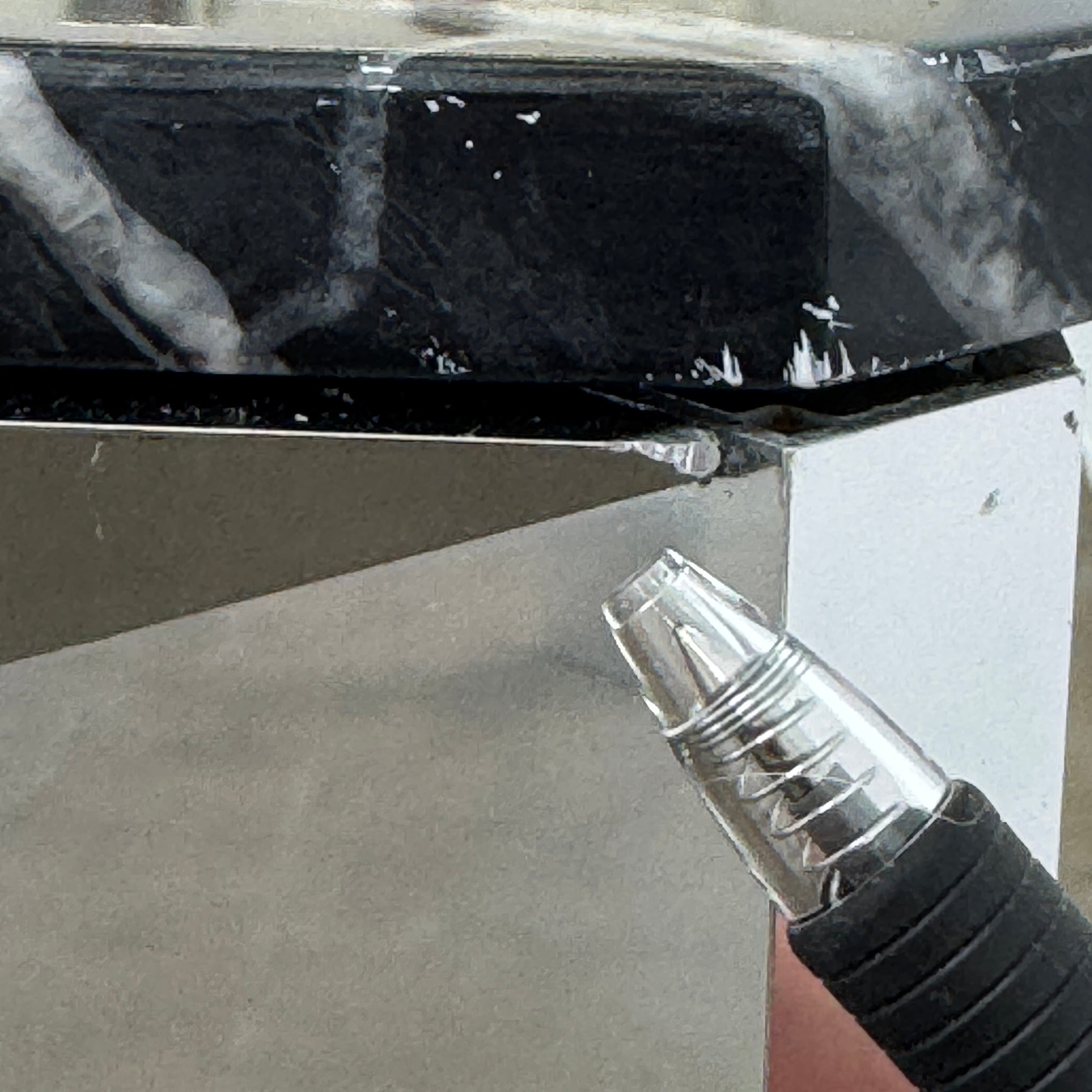 The Molteni & C Diamond table features a rectangular black marble top and angled polished metal legs, set on a brown concrete floor against a plain white wall. This piece by Molteni & C adds sophisticated elegance to any space.