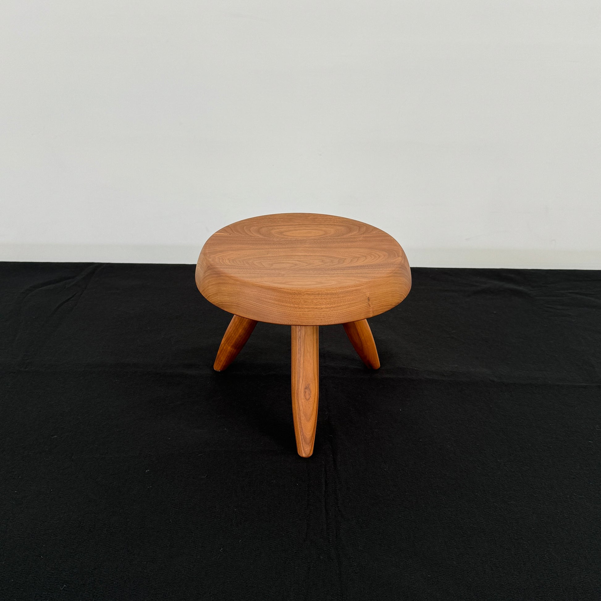 The Cassina “524 Tabouret Berger” stool by Cassina, crafted in walnut with three tapered legs and a round seat, is shown against a plain white background.