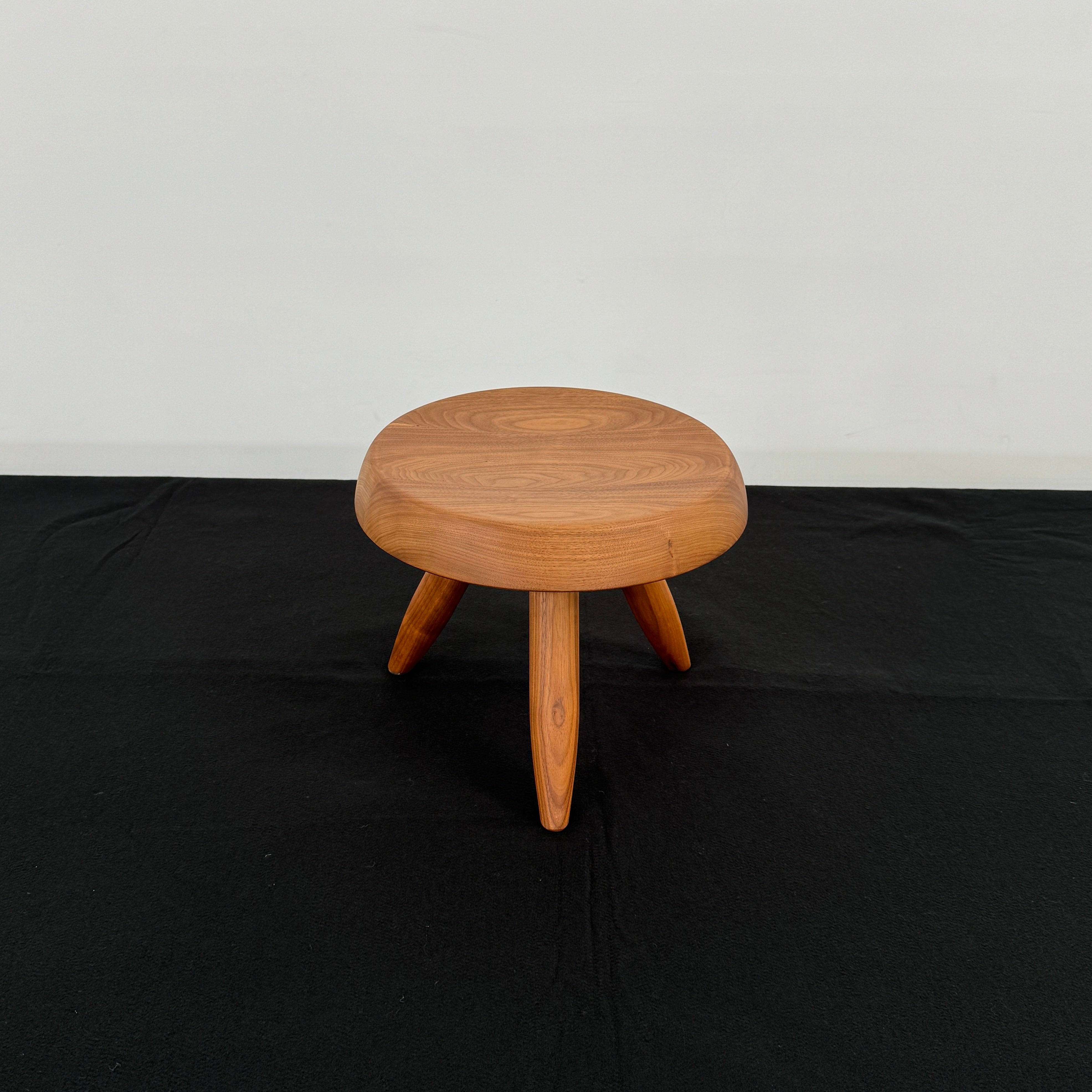 The Cassina “524 Tabouret Berger” stool by Cassina, crafted in walnut with three tapered legs and a round seat, is shown against a plain white background.