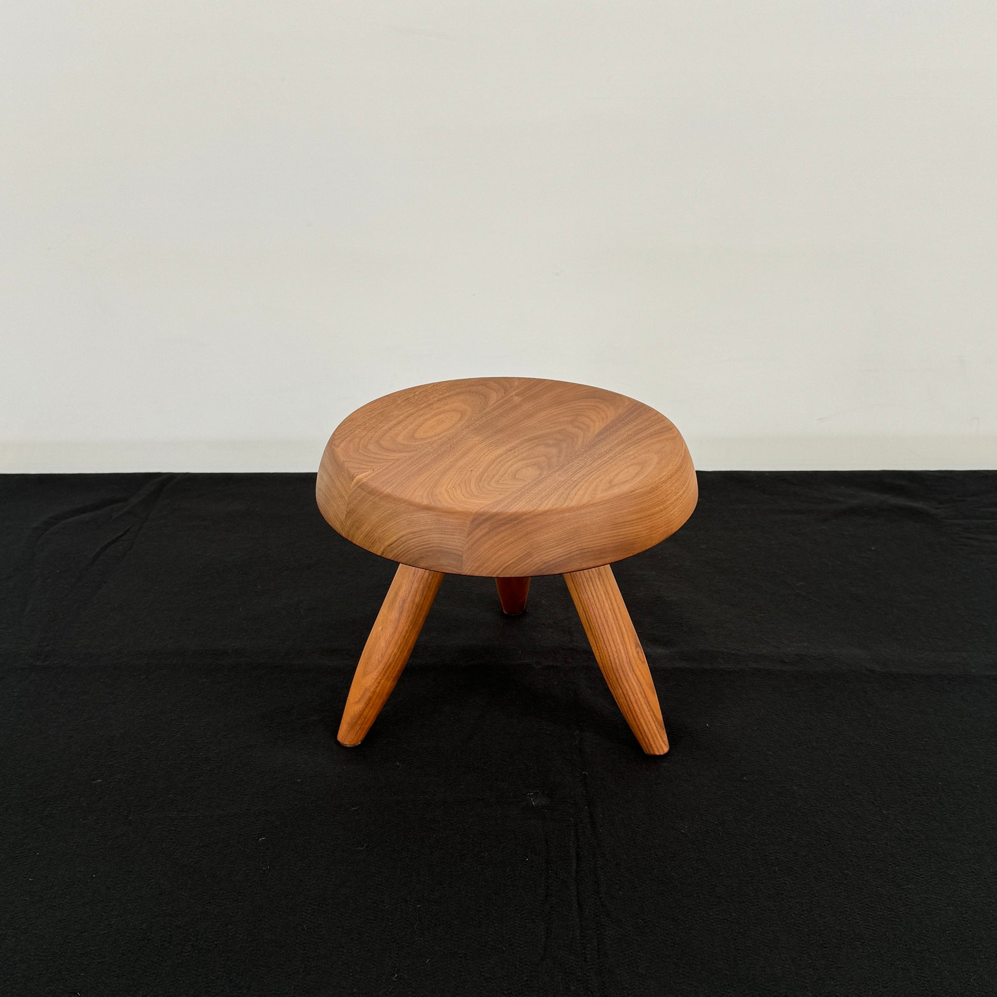 The Cassina “524 Tabouret Berger” stool by Cassina, crafted in walnut with three tapered legs and a round seat, is shown against a plain white background.