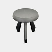 The Cassina 523 Tabouret Meribel by Cassina is a small, round, three-legged solid wood stool with a gray seat and black legs, shown against a plain white background.