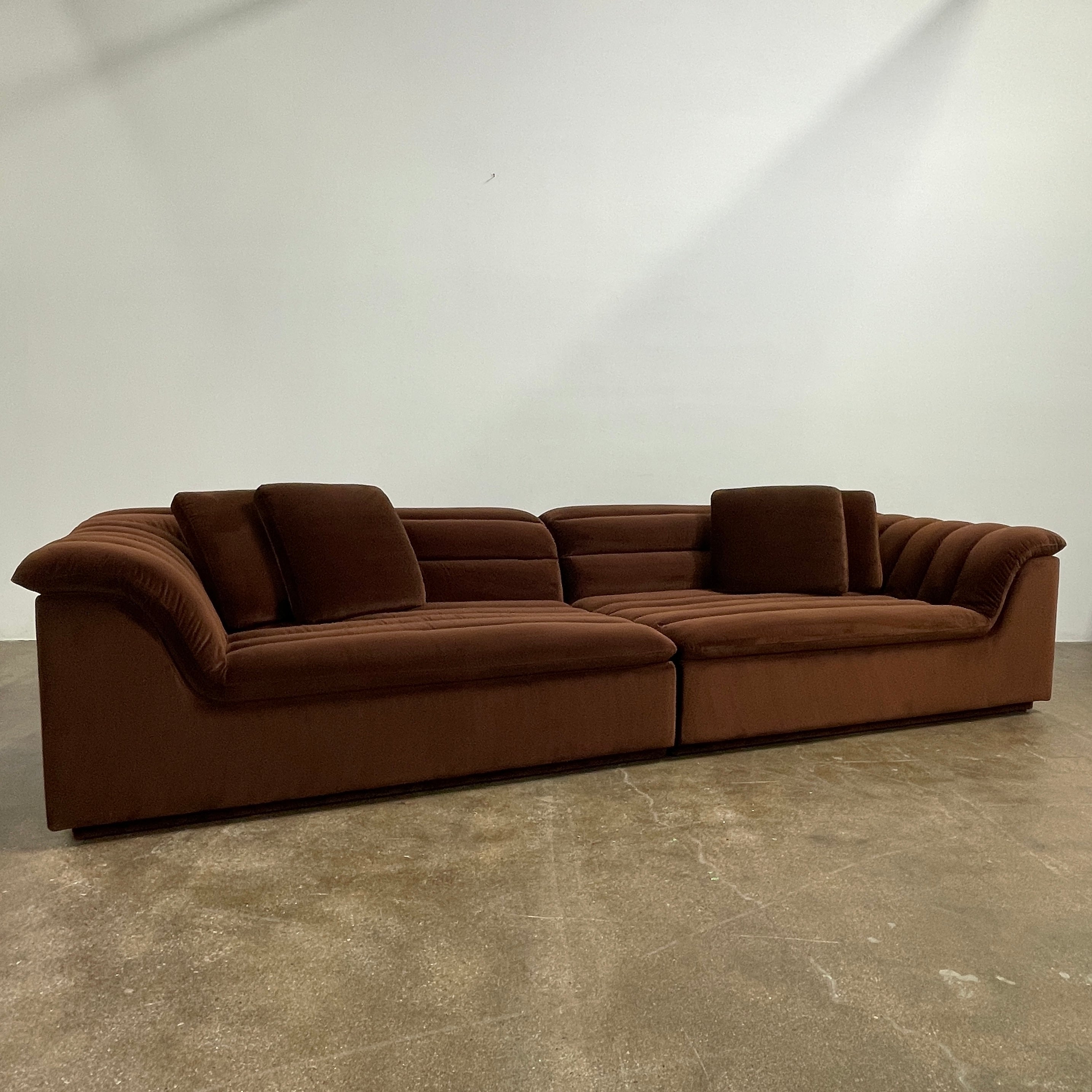 The Ellison Studios Float Sofa is a dark brown sectional from Ellison Studios with velvet upholstery, low profile, channel tufting, and two large cushions for extra comfort.
