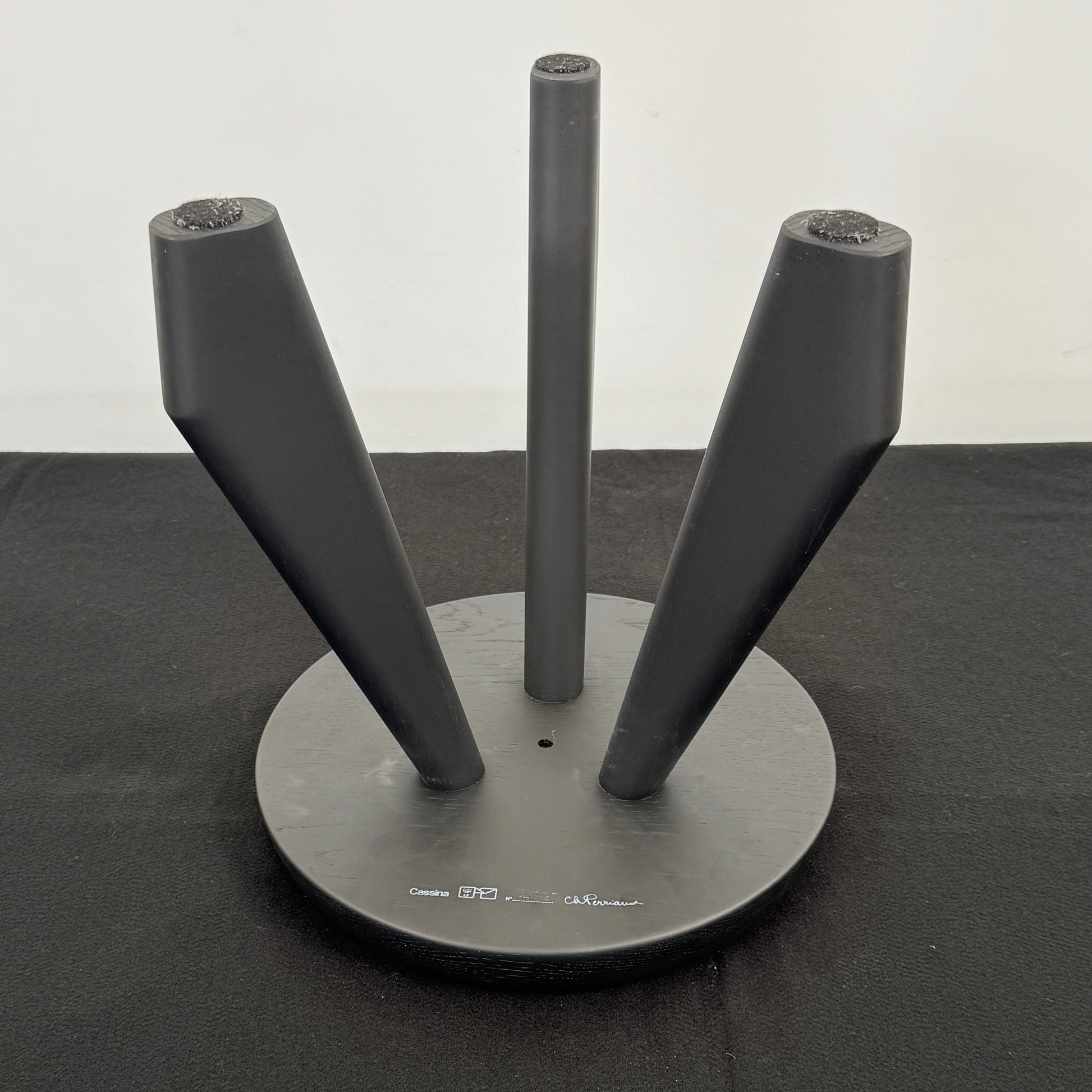 The Cassina 523 Tabouret Meribel by Cassina is a small, round, three-legged solid wood stool with a gray seat and black legs, shown against a plain white background.