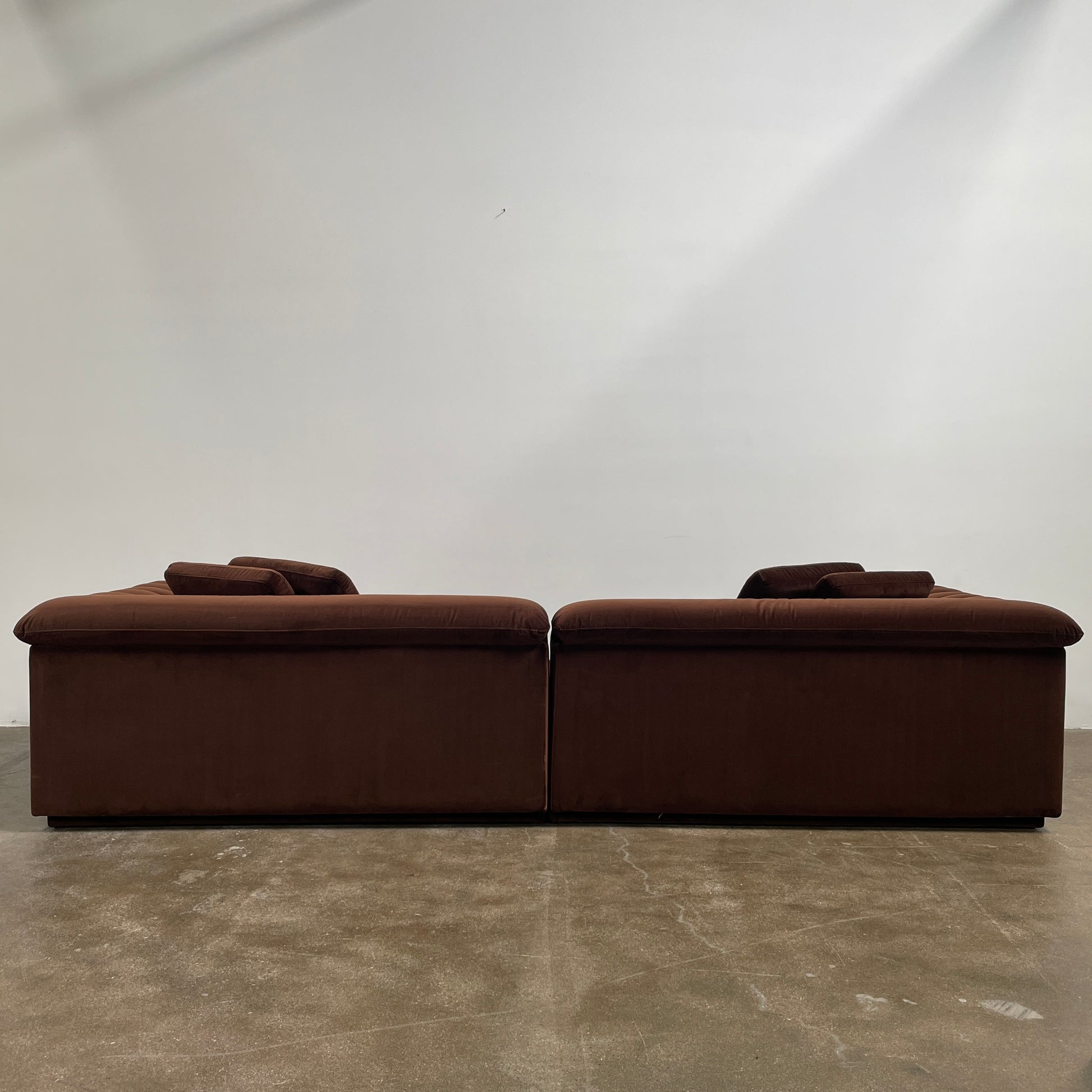 The Ellison Studios Float Sofa is a dark brown sectional from Ellison Studios with velvet upholstery, low profile, channel tufting, and two large cushions for extra comfort.