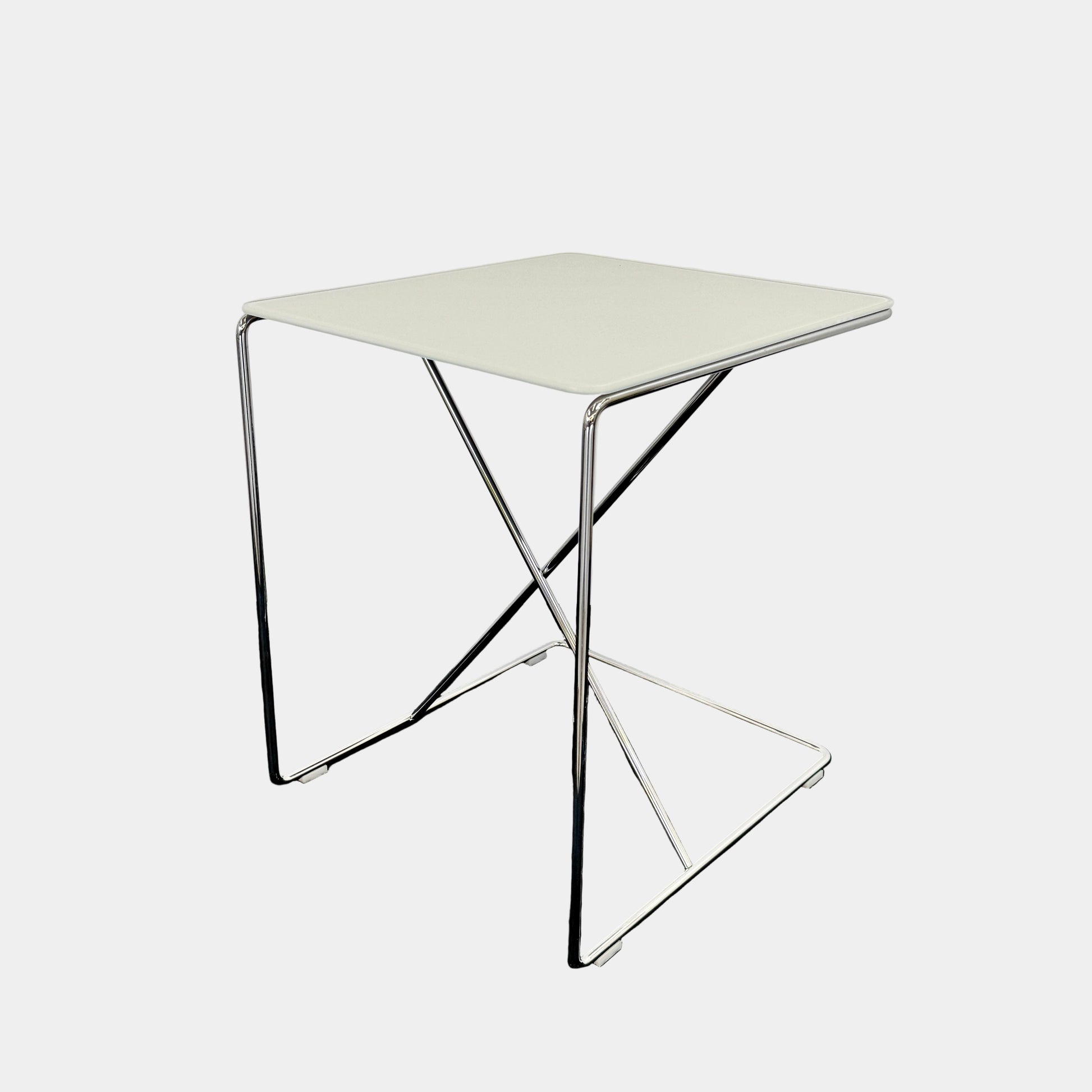 The B&B Italia JJ Cantilever Accent Table by B&B Italia features a white rectangular top and minimalist chrome frame, ideal for modern spaces. Shown against a plain white wall and black floor.