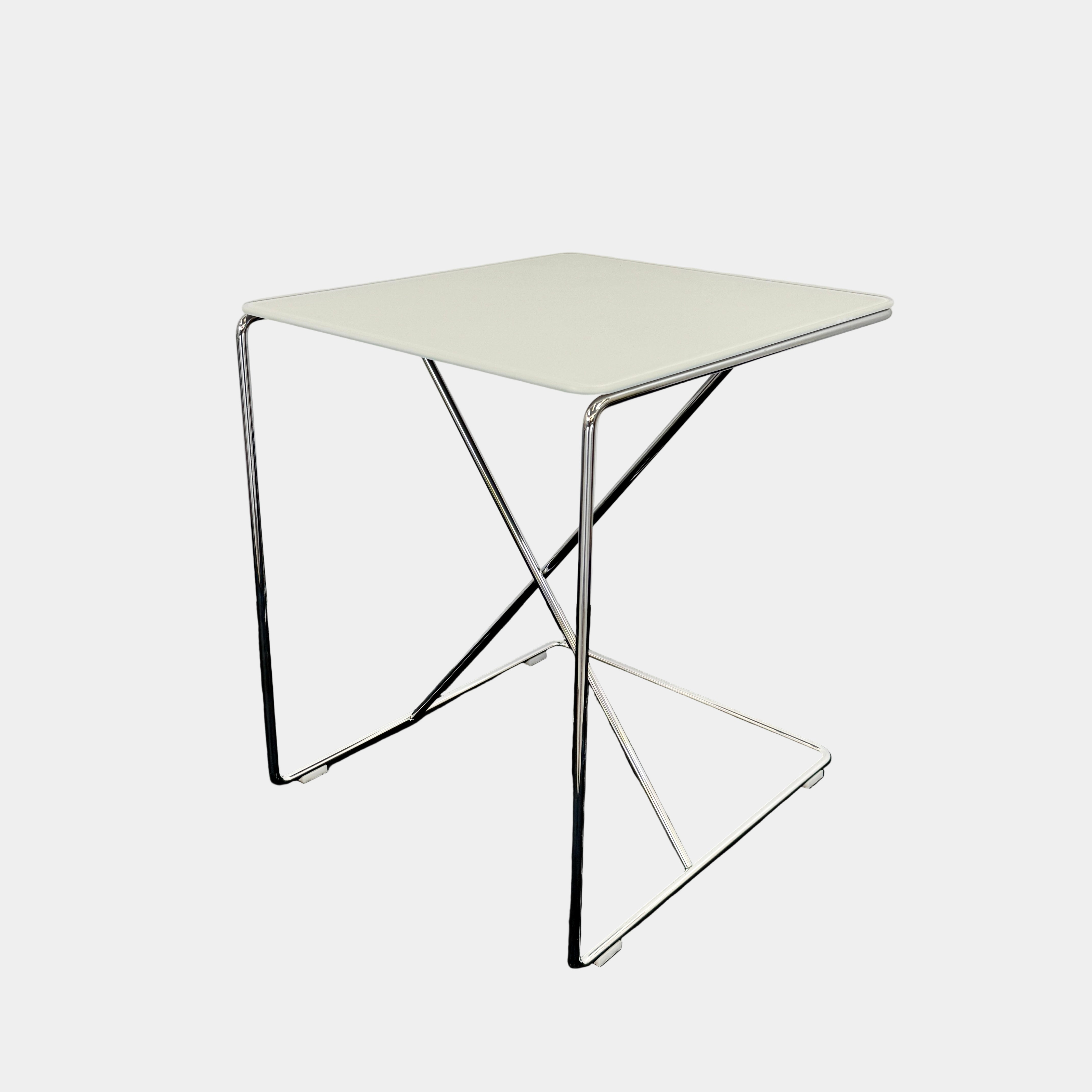 The B&B Italia JJ Cantilever Accent Table by B&B Italia features a white rectangular top and minimalist chrome frame, ideal for modern spaces. Shown against a plain white wall and black floor.
