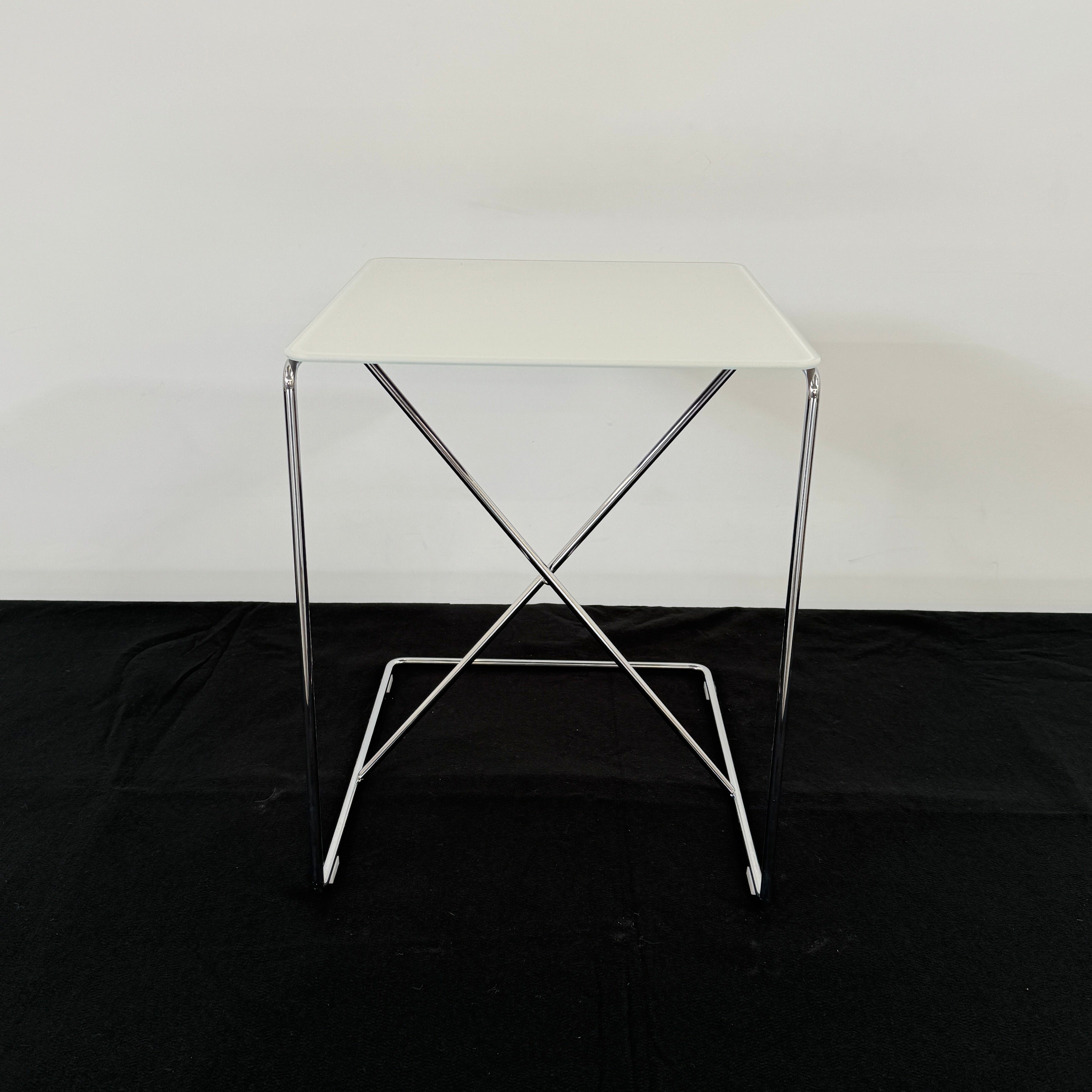 The B&B Italia JJ Cantilever Accent Table by B&B Italia features a white rectangular top and minimalist chrome frame, ideal for modern spaces. Shown against a plain white wall and black floor.