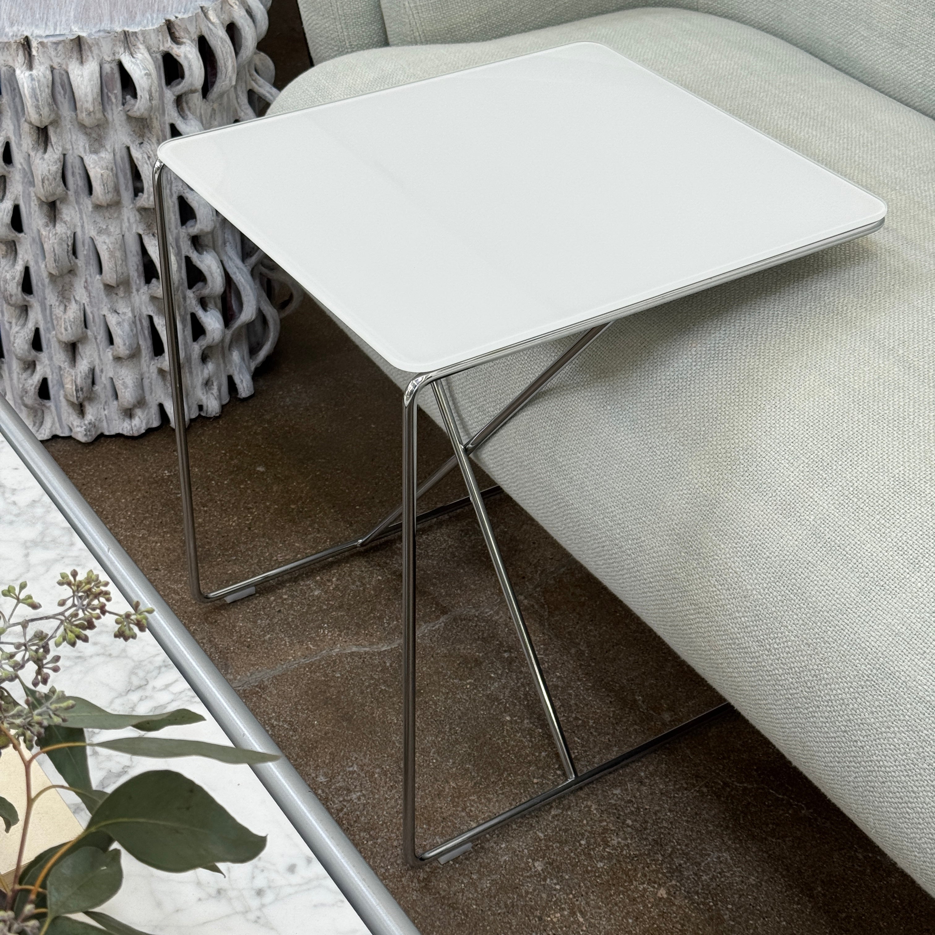 The B&B Italia JJ Cantilever Accent Table by B&B Italia features a white rectangular top and minimalist chrome frame, ideal for modern spaces. Shown against a plain white wall and black floor.