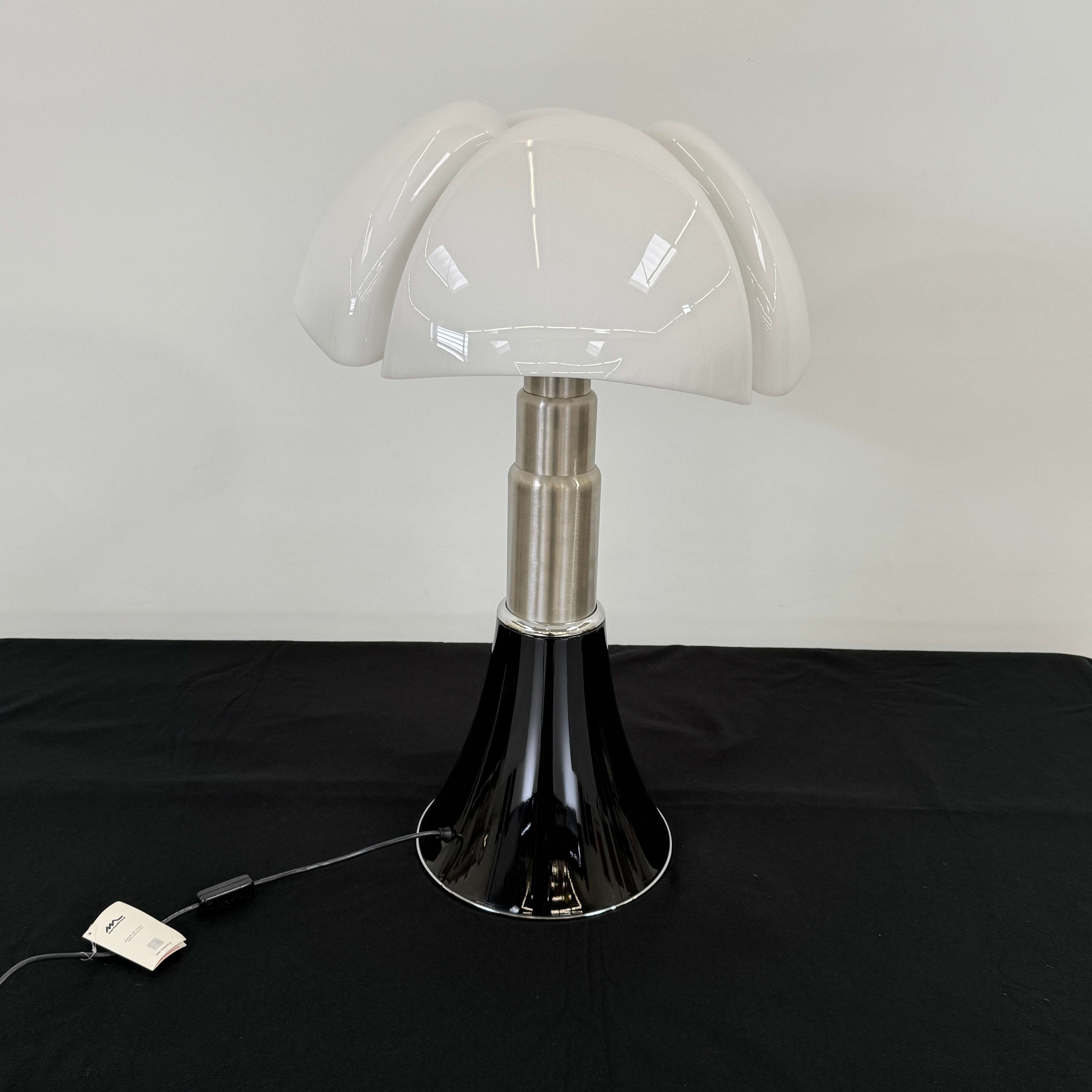 The Martinelli Luce Pipistrello Table Lamp by Martinelli Luce features a black base, silver neck, and white dome-shaped shade, shown against a plain white background with visible power cord and tag.