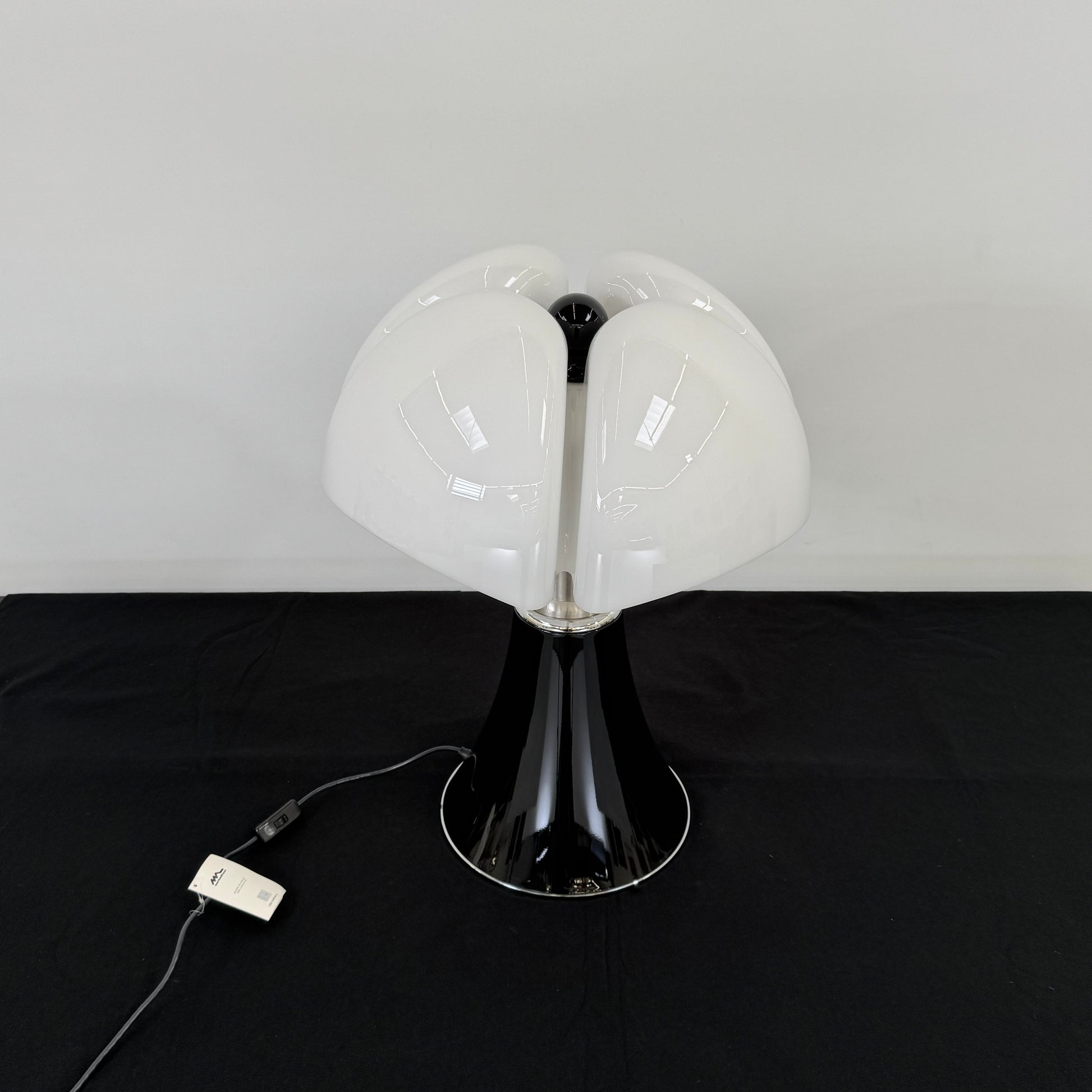The Martinelli Luce Pipistrello Table Lamp by Martinelli Luce features a black base, silver neck, and white dome-shaped shade, shown against a plain white background with visible power cord and tag.