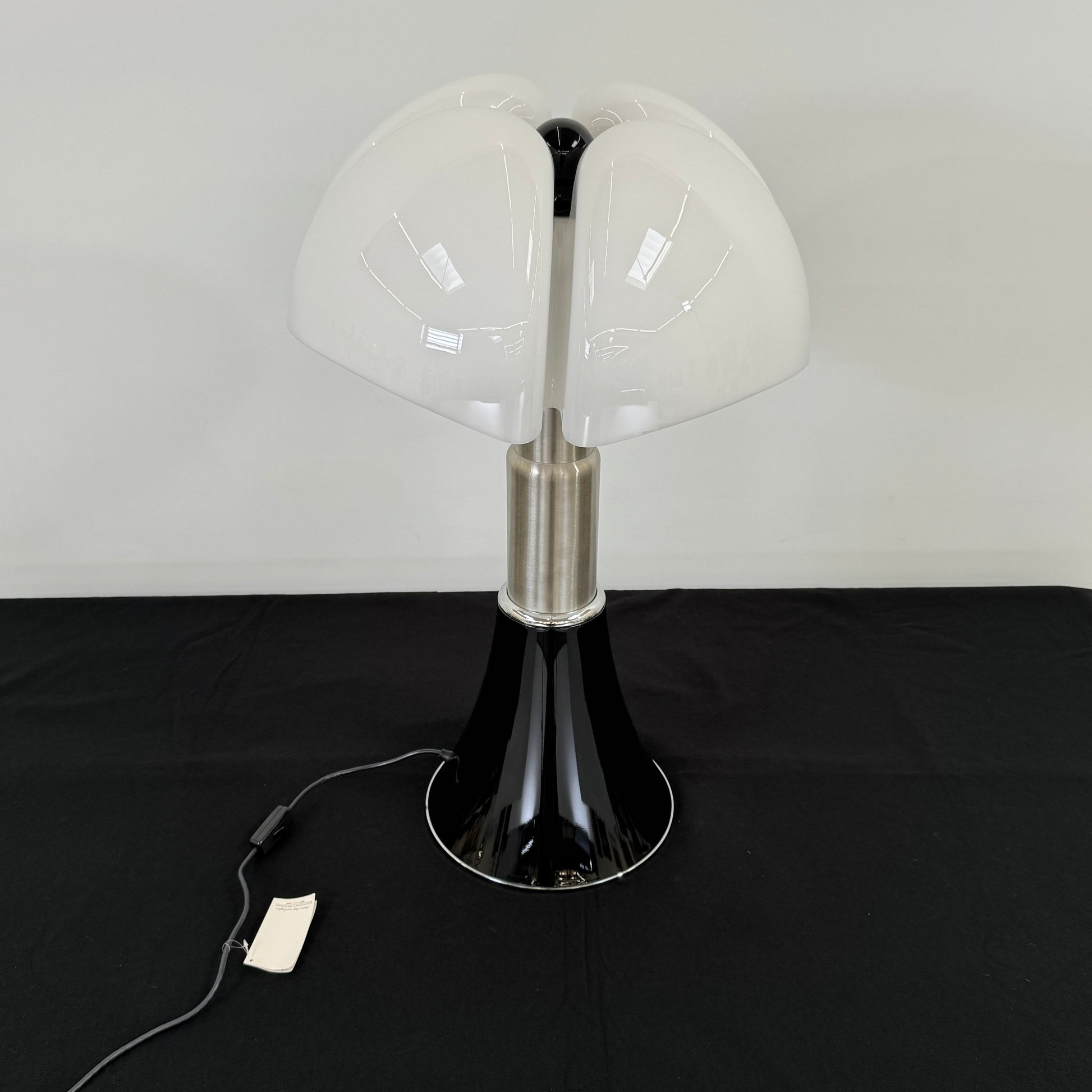 The Martinelli Luce Pipistrello Table Lamp by Martinelli Luce features a black base, silver neck, and white dome-shaped shade, shown against a plain white background with visible power cord and tag.