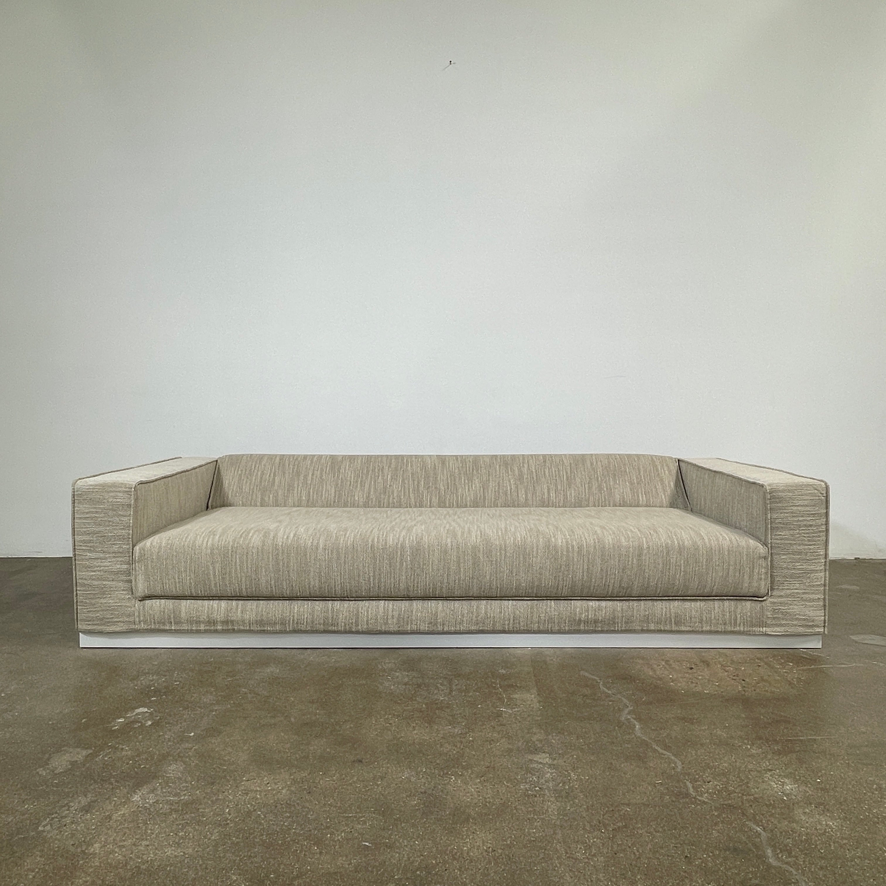 The Tacchini Low Sofa with Convertible Backrest by Tacchini showcases a sleek gray design, clean lines, and rectangular arms, all elegantly set against a crisp white background.