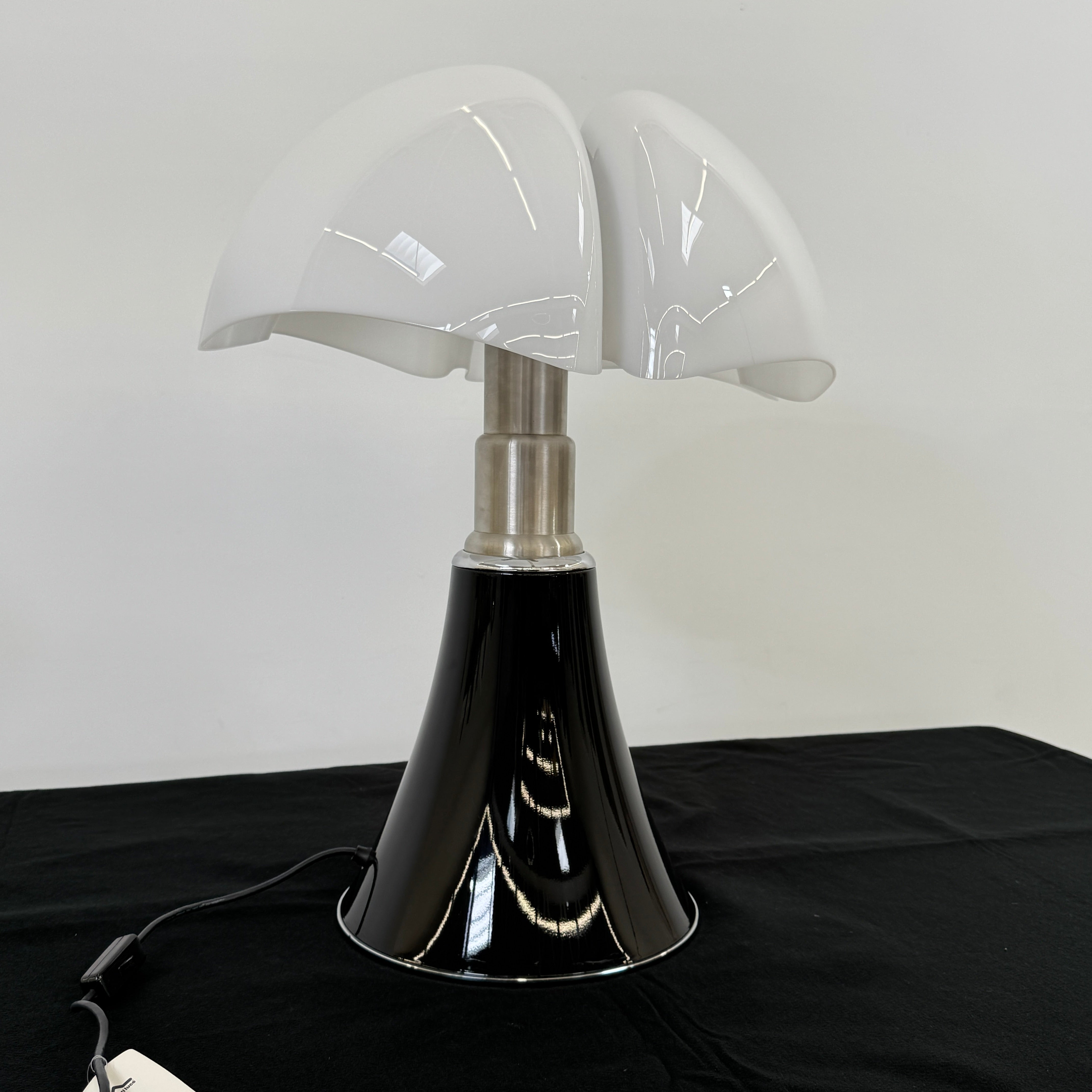 The Martinelli Luce Pipistrello Table Lamp by Martinelli Luce features a black base, silver neck, and white dome-shaped shade, shown against a plain white background with visible power cord and tag.