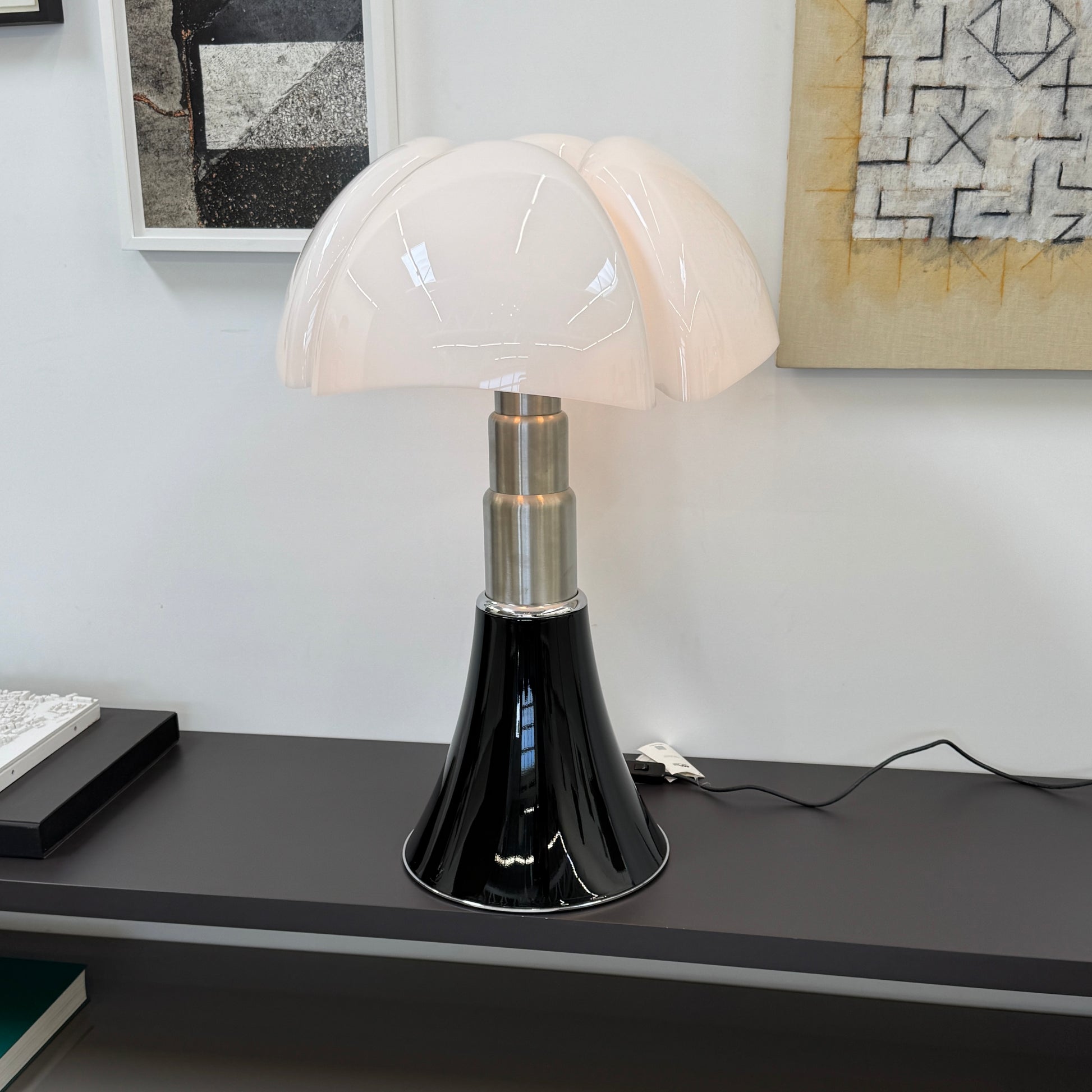 The Martinelli Luce Pipistrello Table Lamp by Martinelli Luce features a black base, silver neck, and white dome-shaped shade, shown against a plain white background with visible power cord and tag.