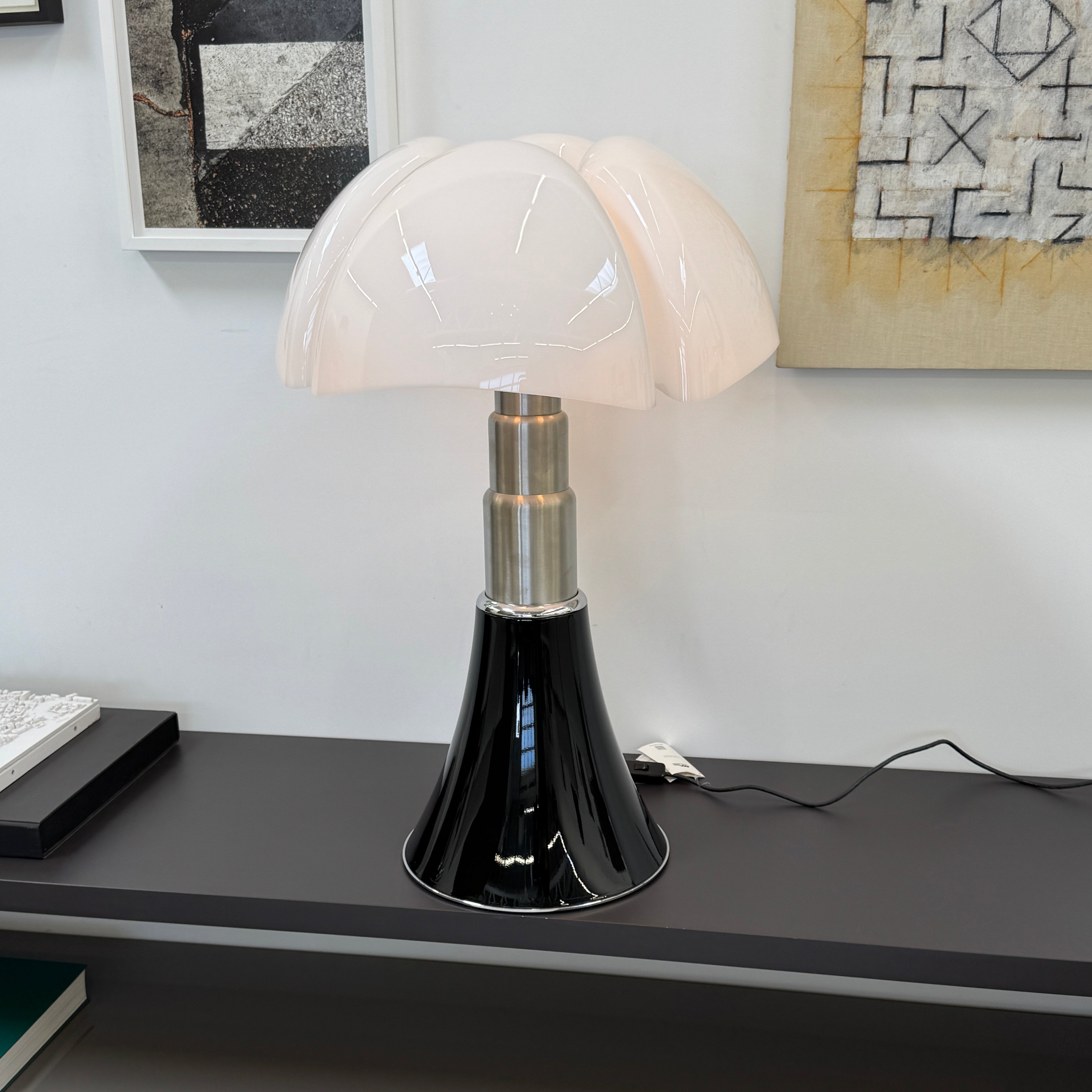 The Martinelli Luce Pipistrello Table Lamp by Martinelli Luce features a black base, silver neck, and white dome-shaped shade, shown against a plain white background with visible power cord and tag.