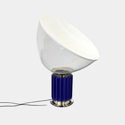 The Flos Taccia LED Table Lamp - Small (HOLD) by Flos, designed by Achille Castiglioni, features a large white bowl-shaped shade and a limited edition blue ribbed cylindrical base, shown against a plain grey background.