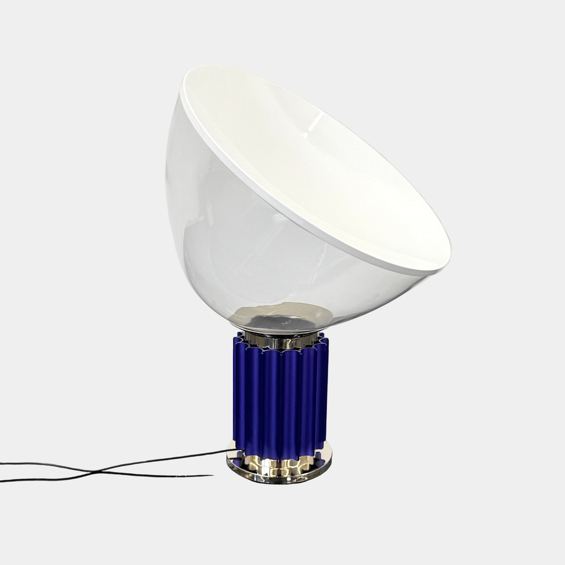 The Flos Taccia LED Table Lamp - Small (HOLD) by Flos, designed by Achille Castiglioni, features a large white bowl-shaped shade and a limited edition blue ribbed cylindrical base, shown against a plain grey background.