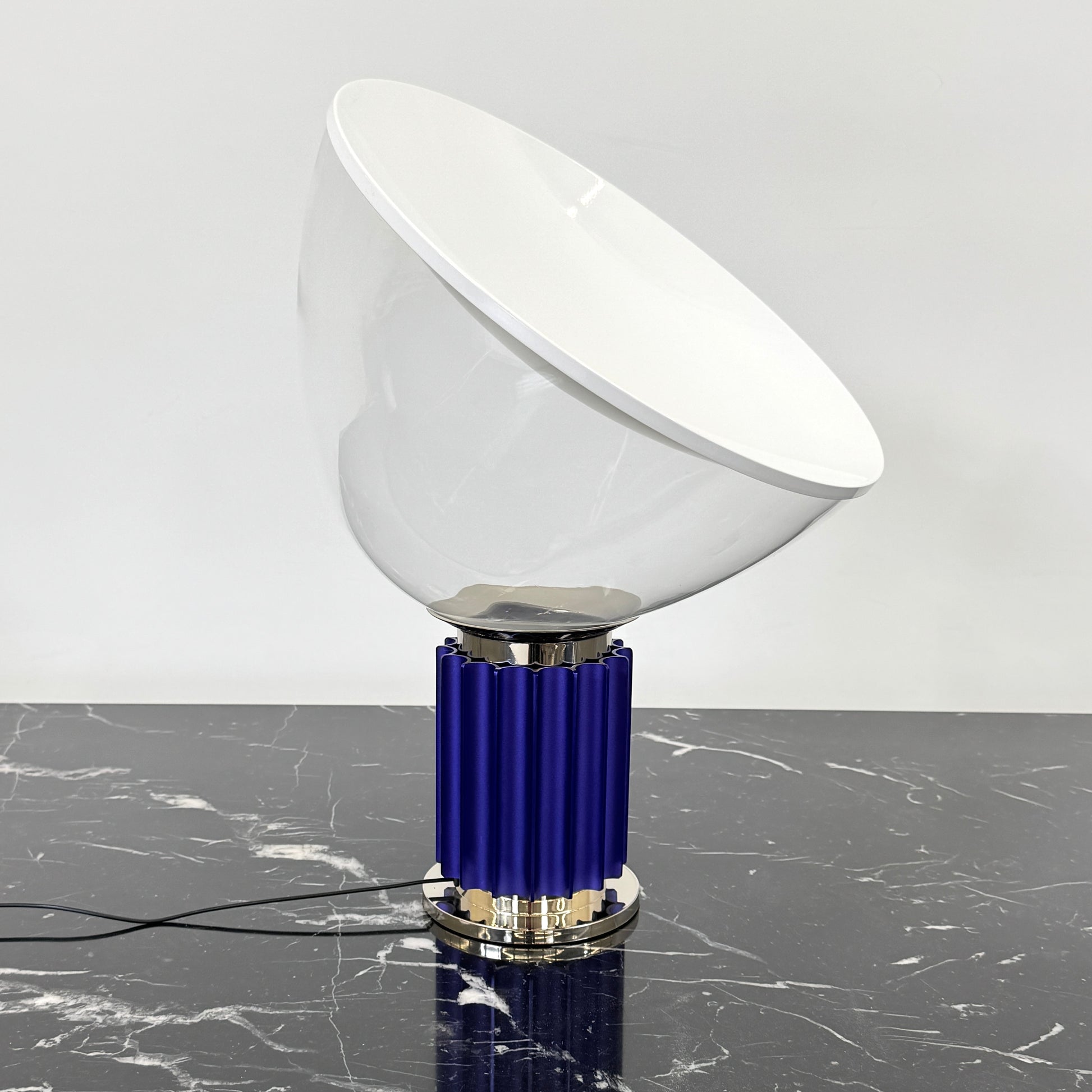 The Flos Taccia LED Table Lamp - Small (HOLD) by Flos, designed by Achille Castiglioni, features a large white bowl-shaped shade and a limited edition blue ribbed cylindrical base, shown against a plain grey background.
