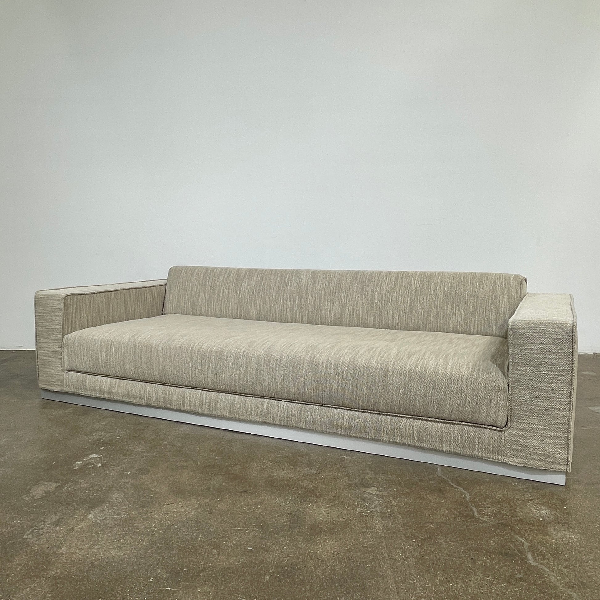 The Tacchini Low Sofa with Convertible Backrest by Tacchini showcases a sleek gray design, clean lines, and rectangular arms, all elegantly set against a crisp white background.