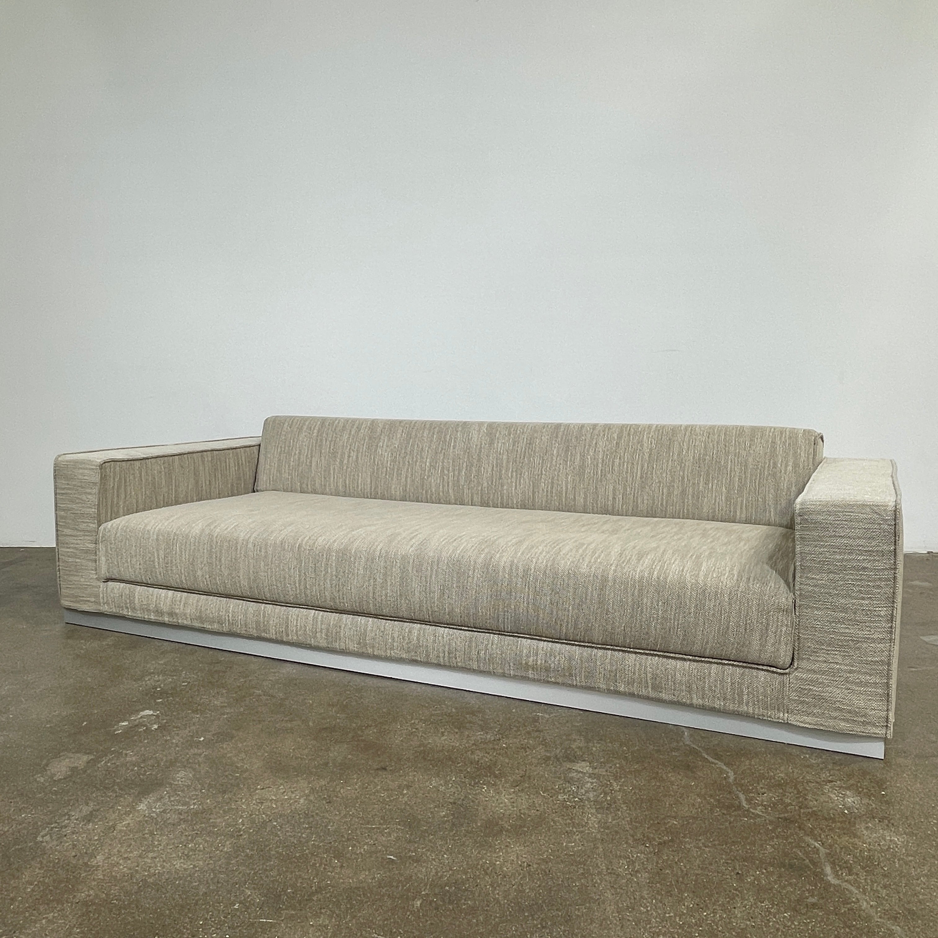 The Tacchini Low Sofa with Convertible Backrest by Tacchini showcases a sleek gray design, clean lines, and rectangular arms, all elegantly set against a crisp white background.