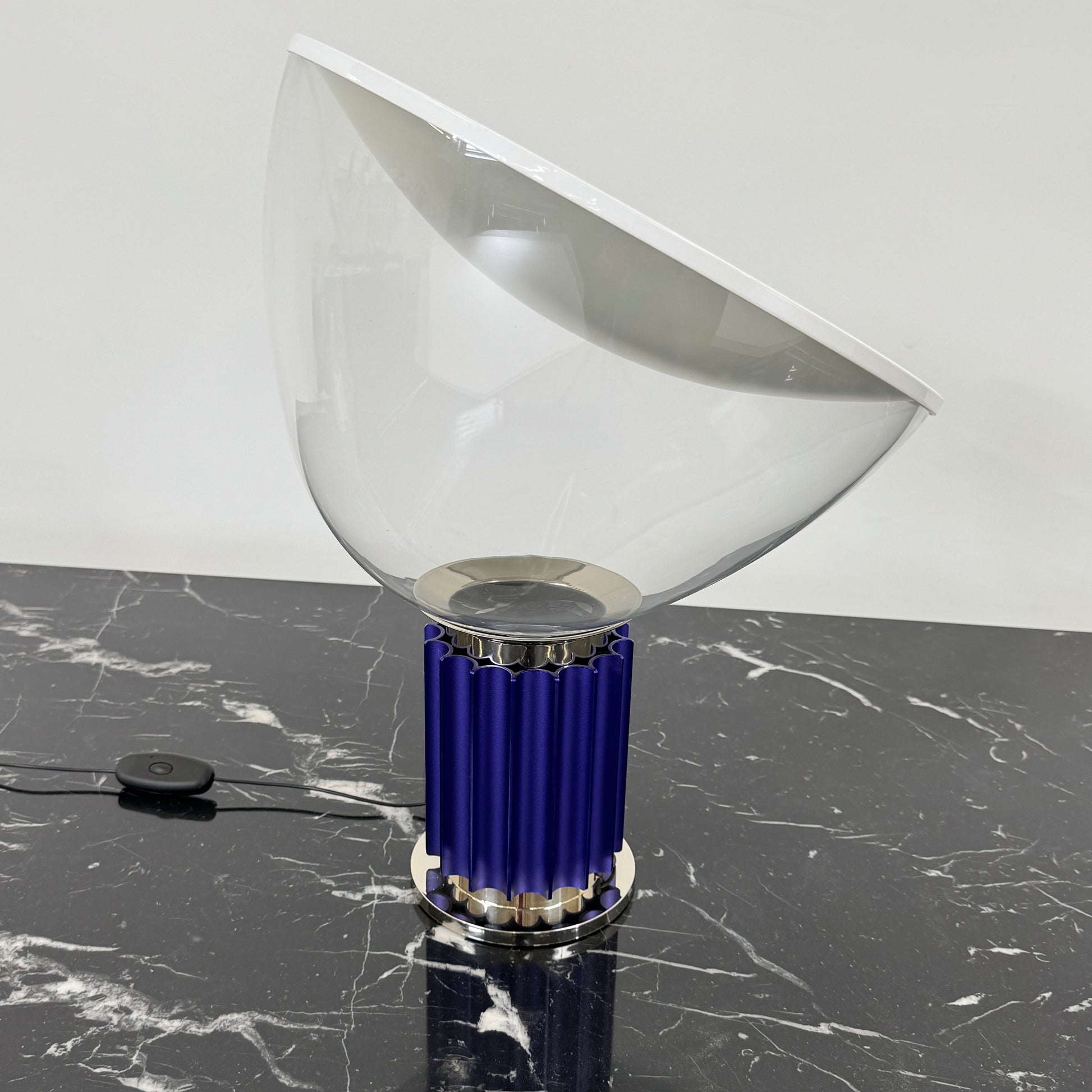 The Flos Taccia LED Table Lamp - Small (HOLD) by Flos, designed by Achille Castiglioni, features a large white bowl-shaped shade and a limited edition blue ribbed cylindrical base, shown against a plain grey background.