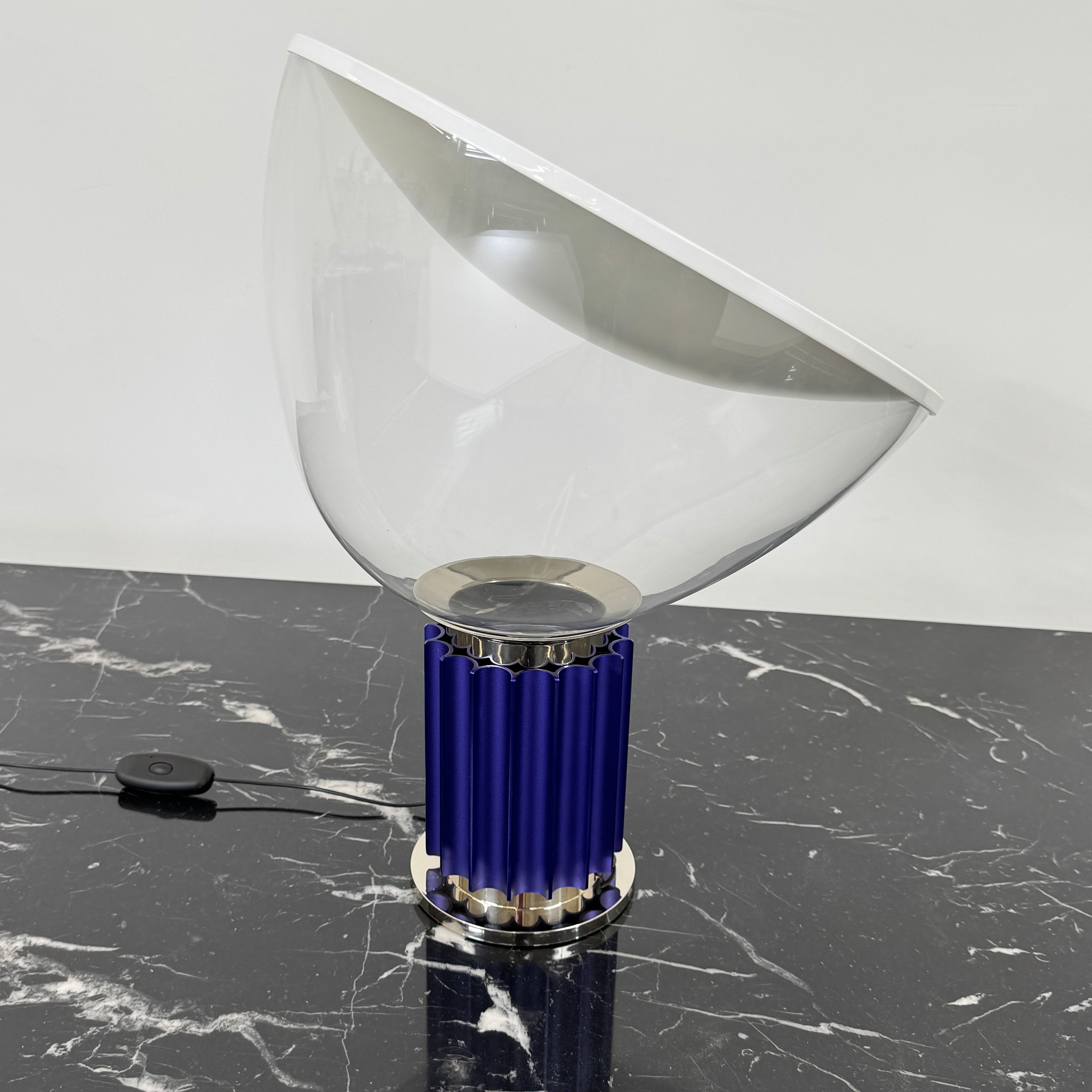 The Flos Taccia LED Table Lamp - Small (HOLD) by Flos, designed by Achille Castiglioni, features a large white bowl-shaped shade and a limited edition blue ribbed cylindrical base, shown against a plain grey background.