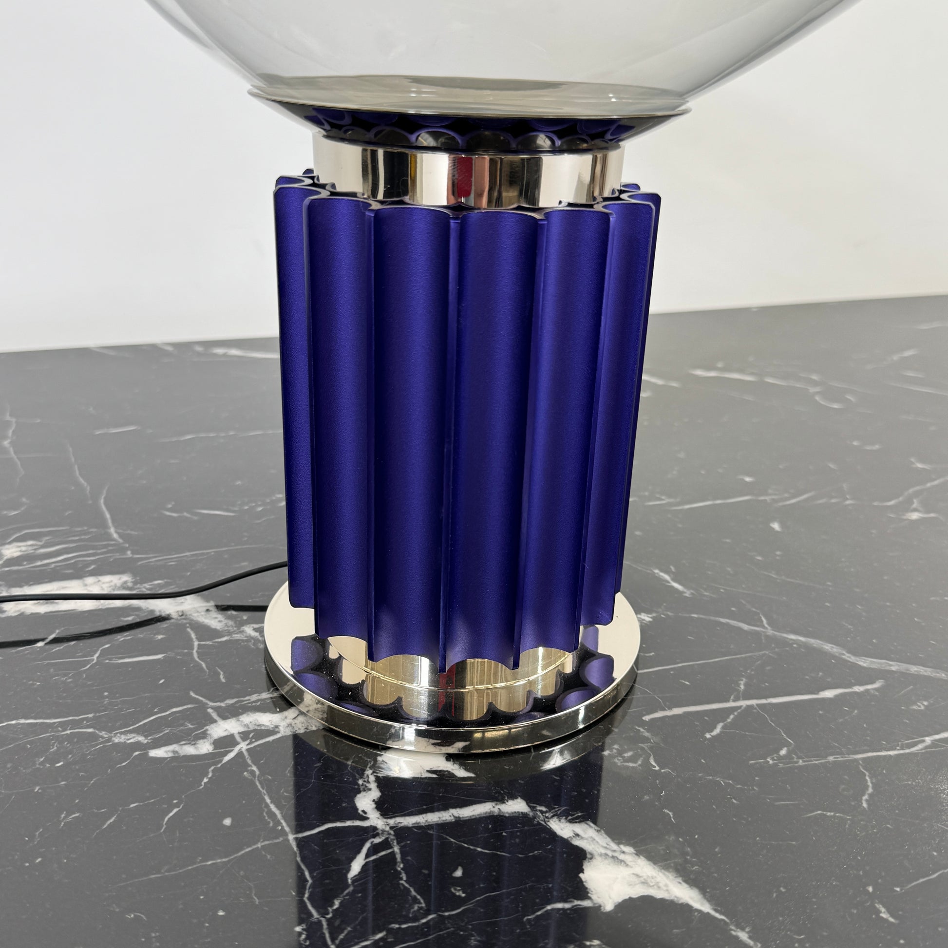 The Flos Taccia LED Table Lamp - Small (HOLD) by Flos, designed by Achille Castiglioni, features a large white bowl-shaped shade and a limited edition blue ribbed cylindrical base, shown against a plain grey background.