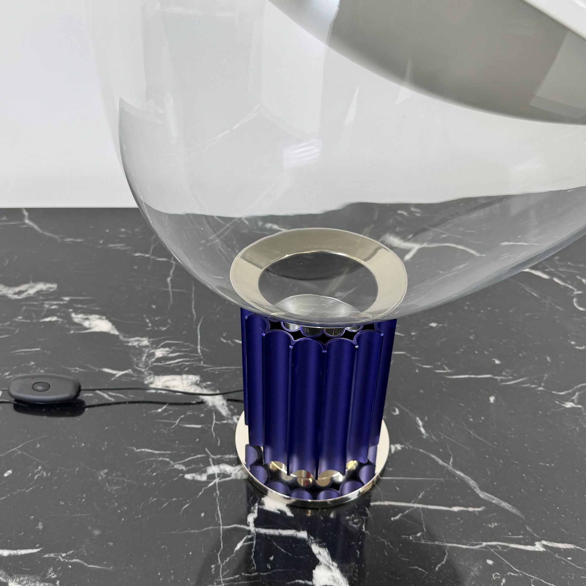 The Flos Taccia LED Table Lamp - Small (HOLD) by Flos, designed by Achille Castiglioni, features a large white bowl-shaped shade and a limited edition blue ribbed cylindrical base, shown against a plain grey background.