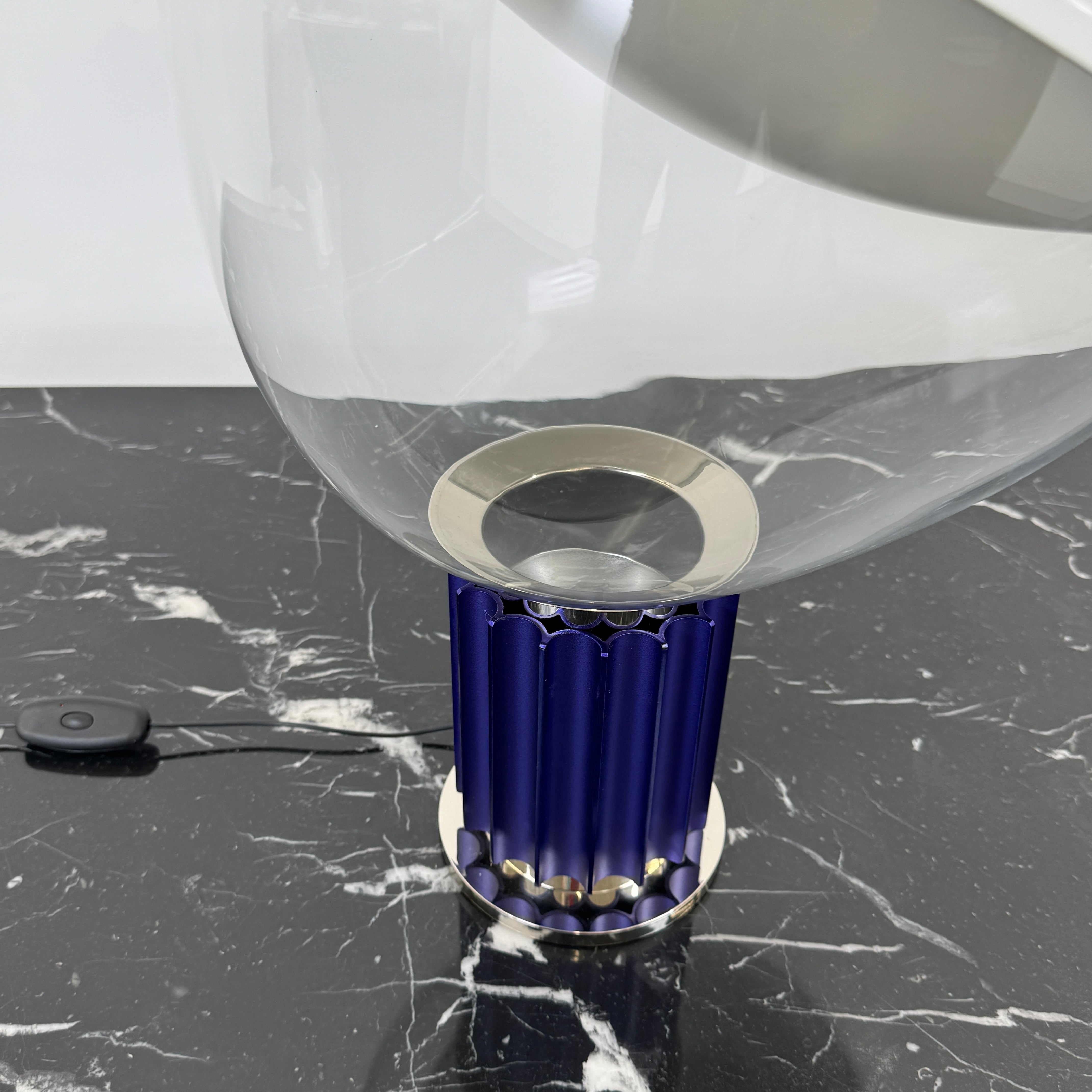 The Flos Taccia LED Table Lamp - Small (HOLD) by Flos, designed by Achille Castiglioni, features a large white bowl-shaped shade and a limited edition blue ribbed cylindrical base, shown against a plain grey background.