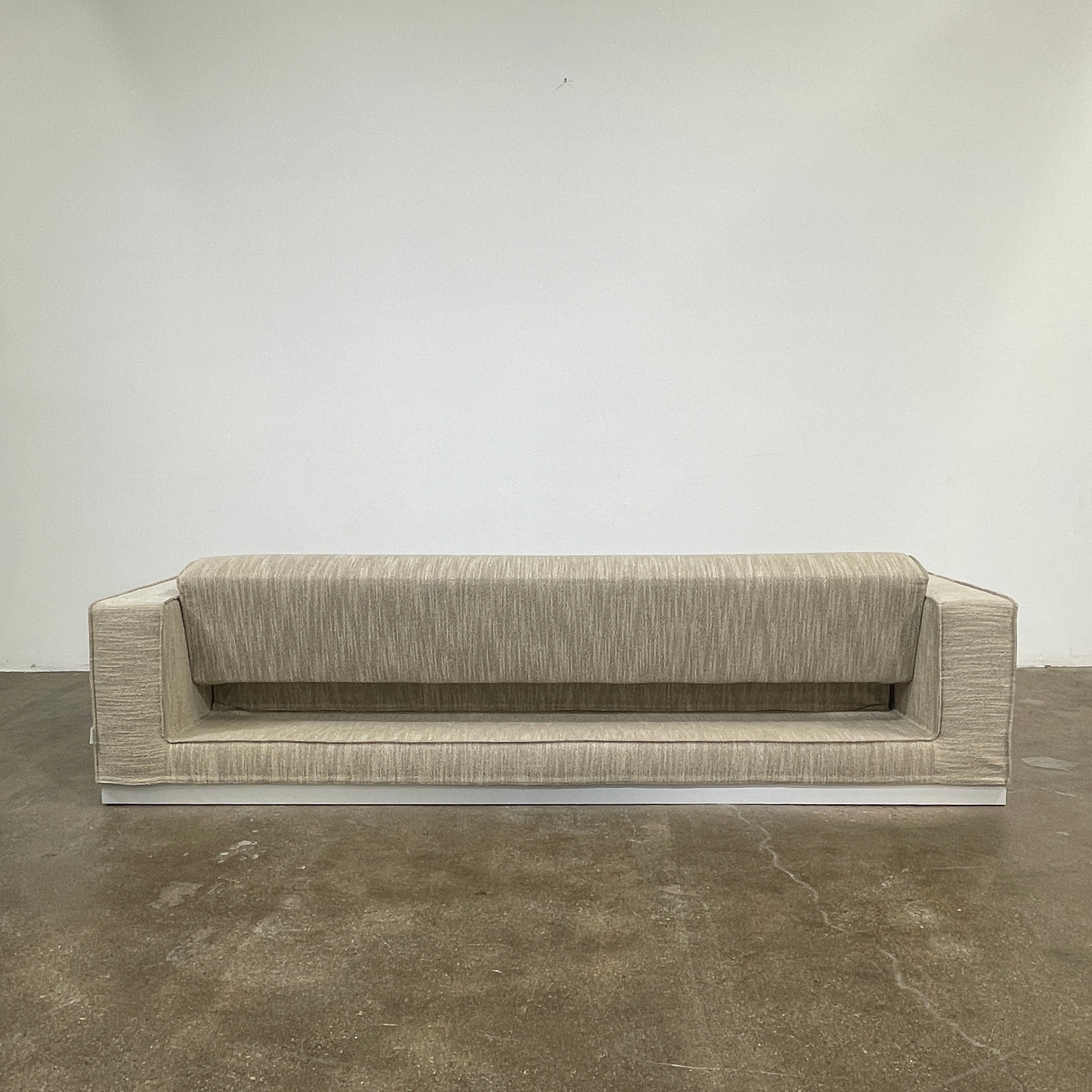 The Tacchini Low Sofa with Convertible Backrest by Tacchini showcases a sleek gray design, clean lines, and rectangular arms, all elegantly set against a crisp white background.