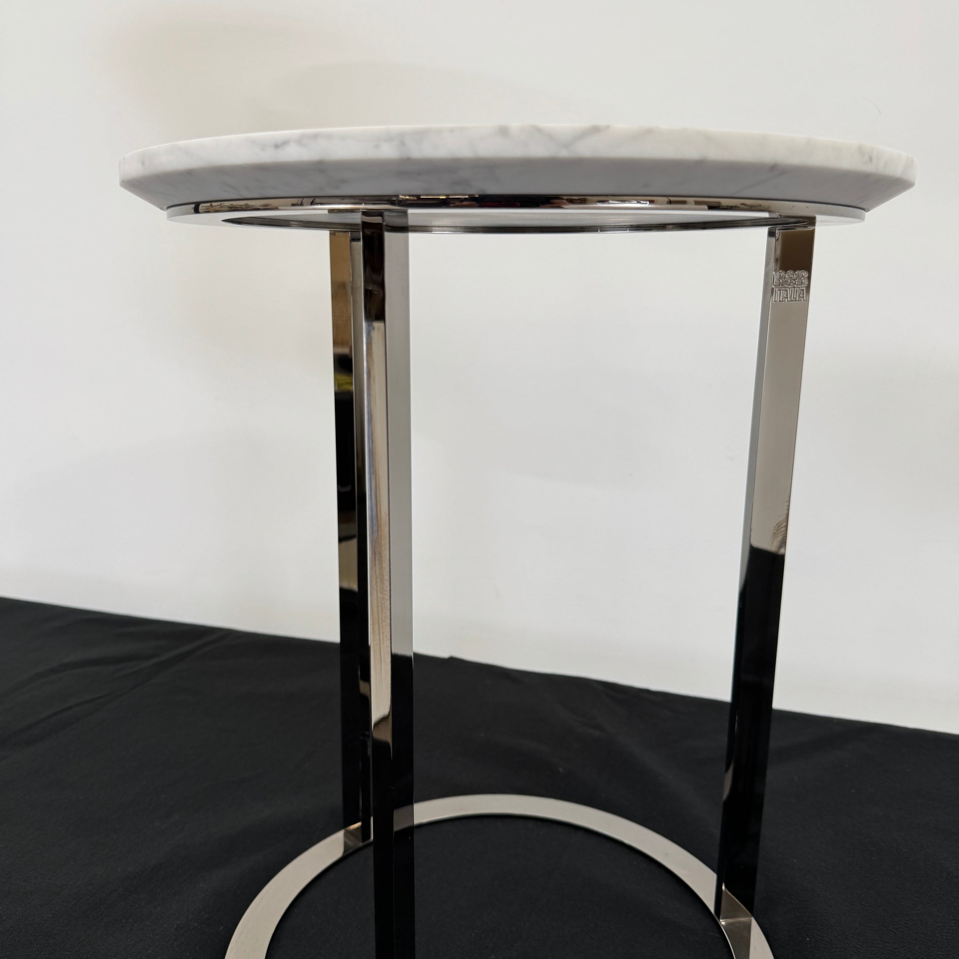The B&B Italia Mera Accent Table features a round Carrara marble top and a three-legged metal frame with a circular base, showcasing B&B Italia's signature elegance.