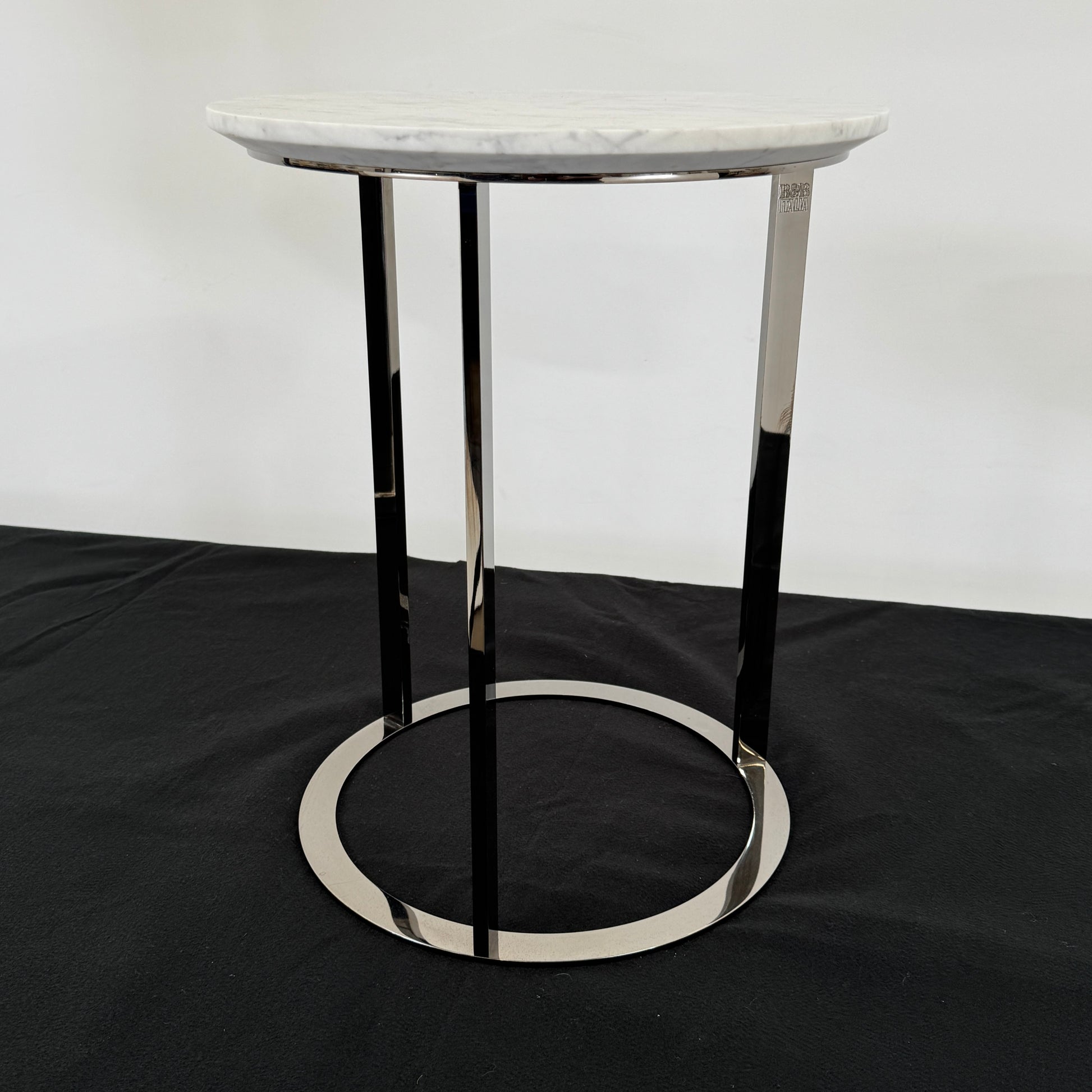 The B&B Italia Mera Accent Table features a round Carrara marble top and a three-legged metal frame with a circular base, showcasing B&B Italia's signature elegance.