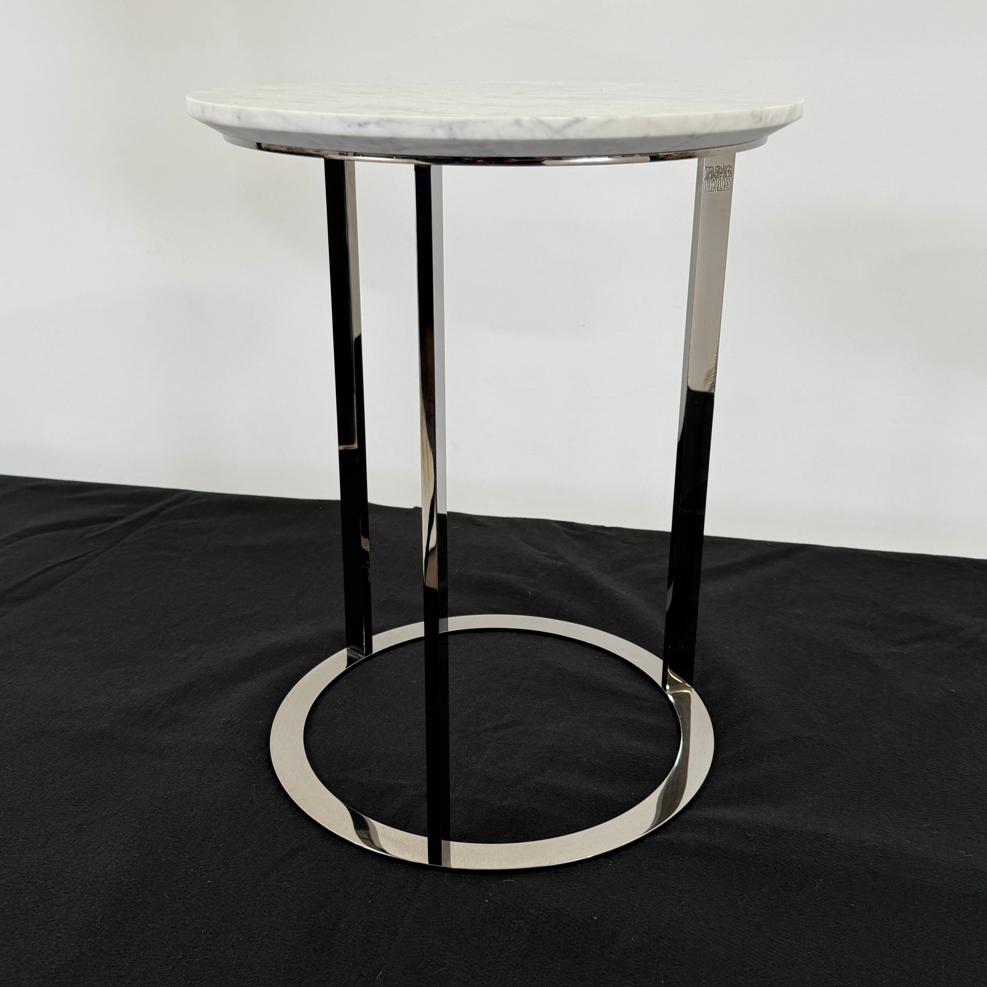 The B&B Italia Mera Accent Table features a round Carrara marble top and a three-legged metal frame with a circular base, showcasing B&B Italia's signature elegance.