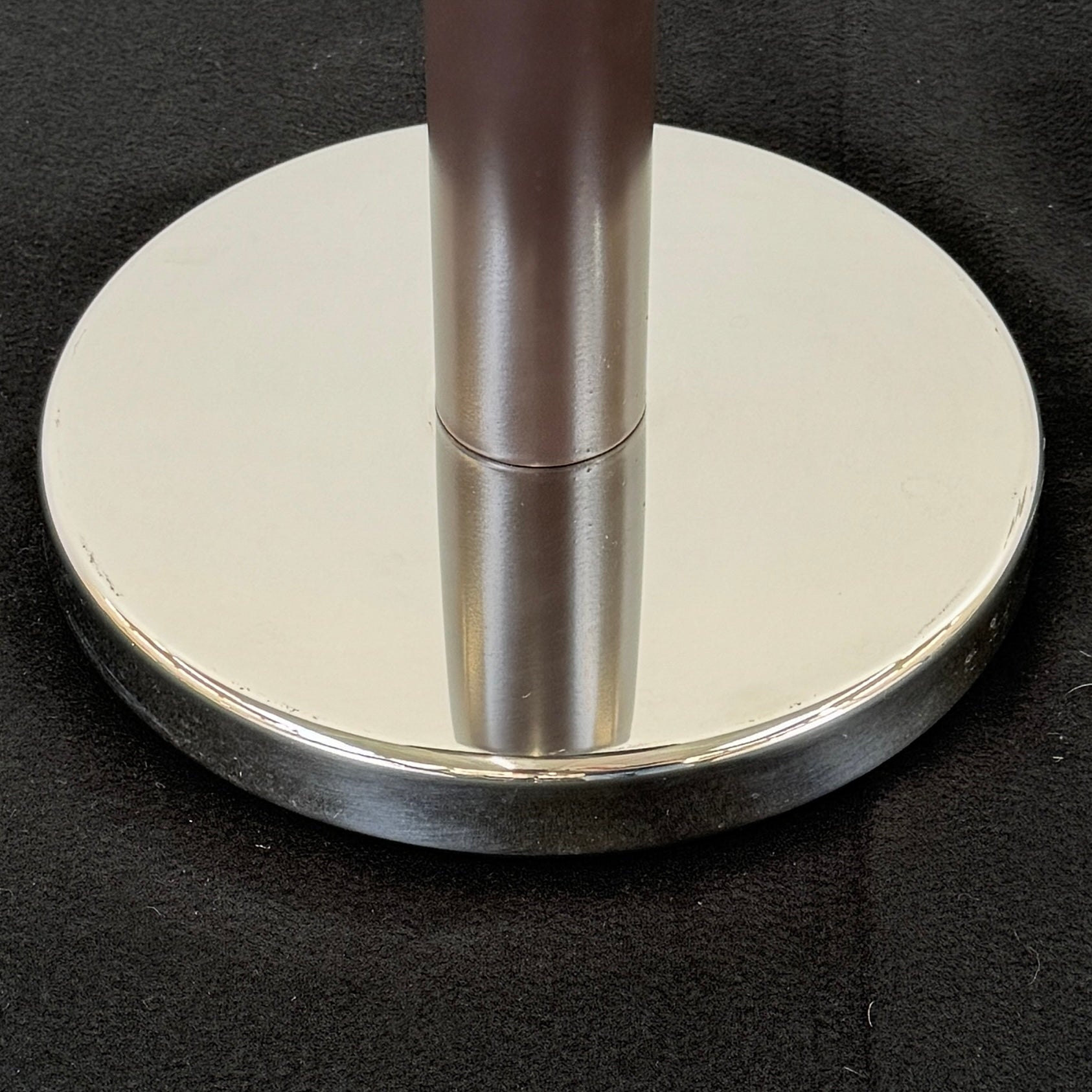 The Alessi Ettore Sottsass Wine Cooler and Stand features a stainless steel cooler with handles, mounted on a tall circular-base stand, and is set against a plain background.