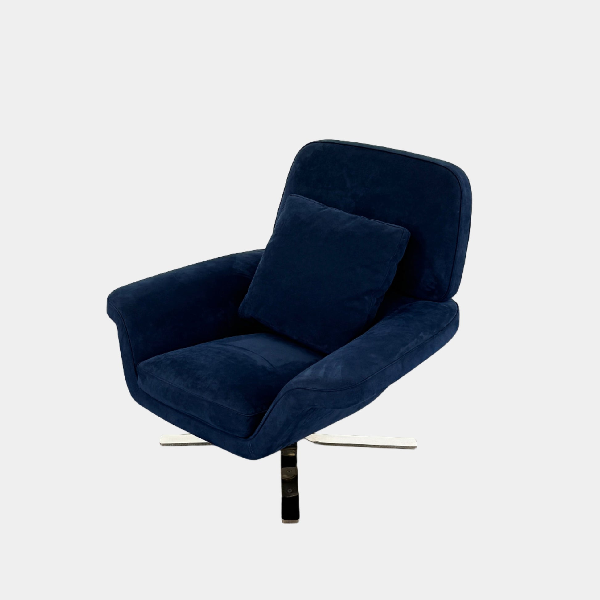 The Minotti Blake Swivel Armchair in modern navy blue, featuring a matching cushion and metal swivel base, is placed on a bare concrete floor against a plain white wall.