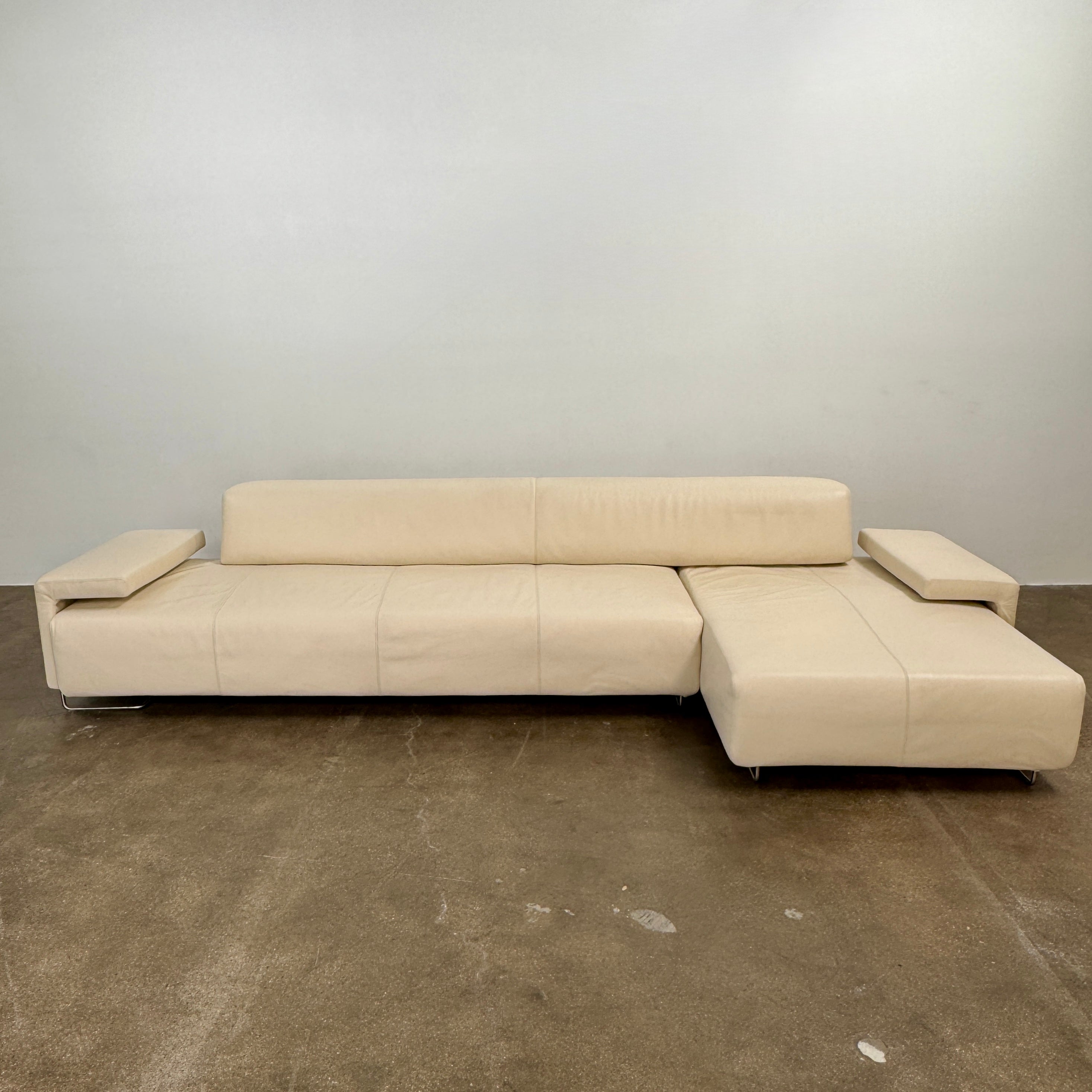 The Moroso Lowland Sectional Sofa by Moroso features beige leather, a low backrest, wide armrests, and a right-side chaise lounge inspired by Patricia Urquiola’s modern design, set against a plain white background.