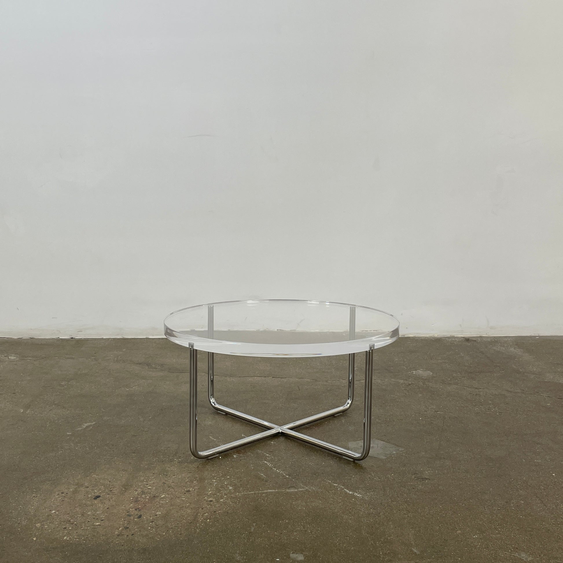 The Minotti Lucite Accent Table boasts a round glass top with a chrome metal frame and crossed base, capturing the Italian elegance synonymous with Minotti's design.