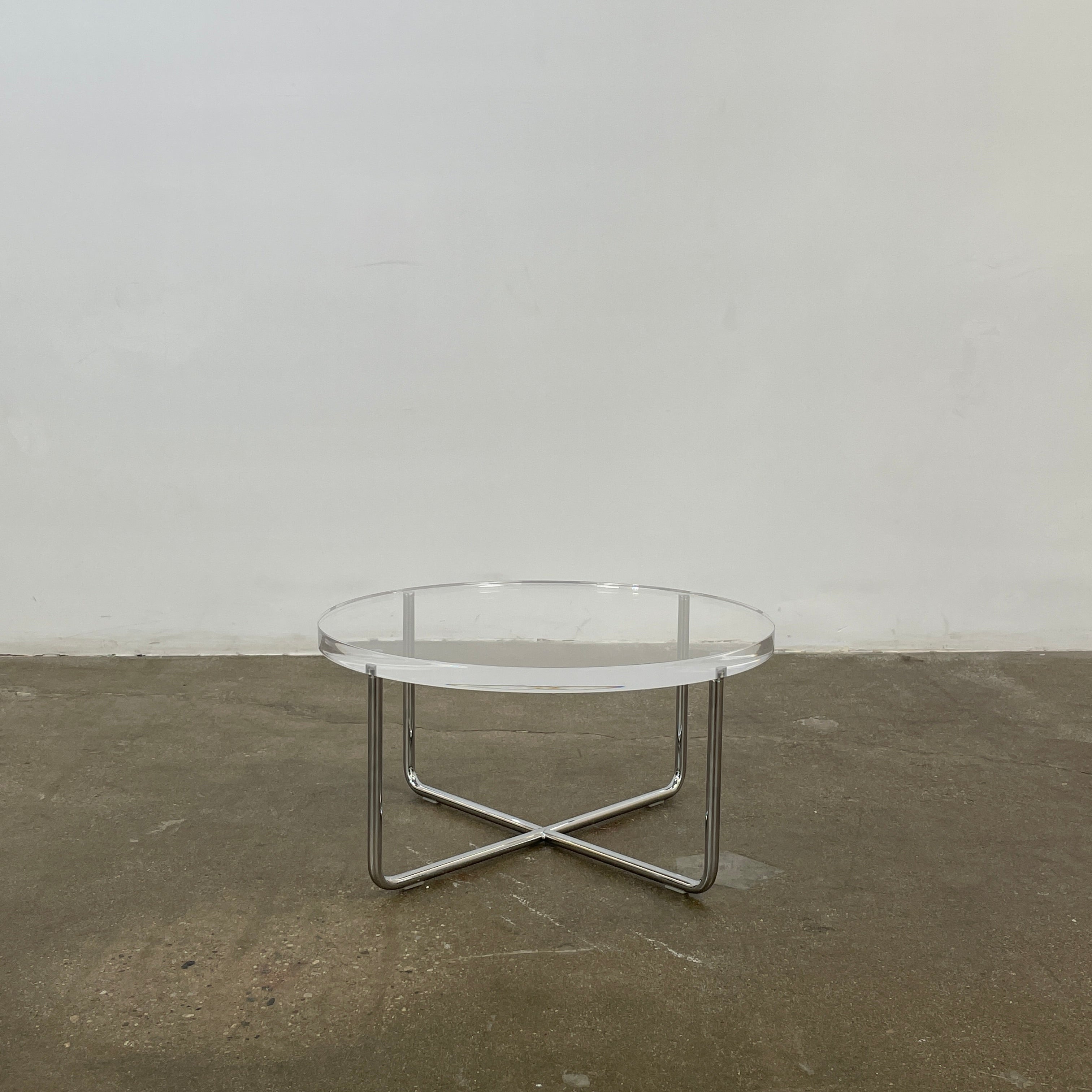 The Minotti Lucite Accent Table boasts a round glass top with a chrome metal frame and crossed base, capturing the Italian elegance synonymous with Minotti's design.