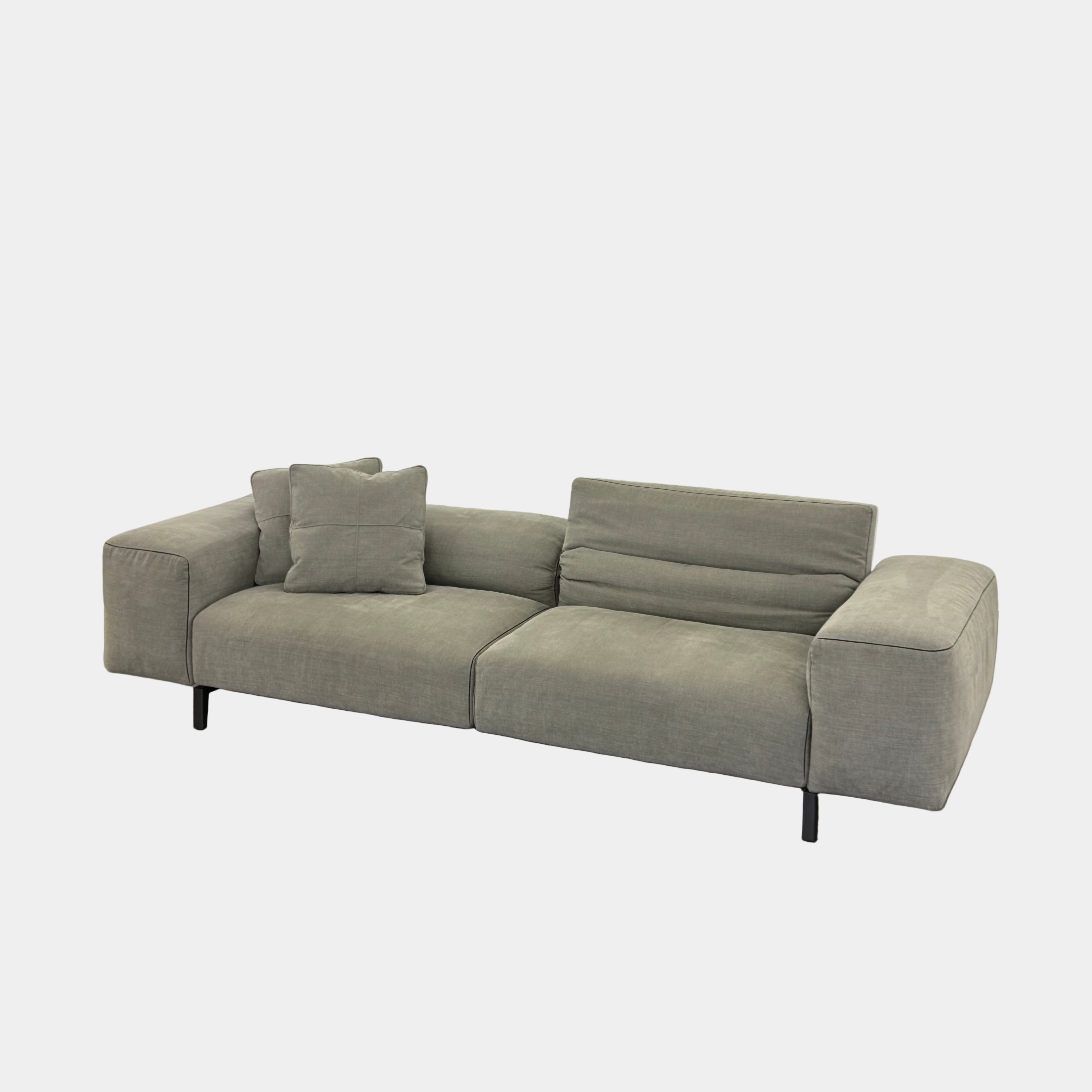 A modern Cassina Scighera Sofa by Cassina, in light gray with two matching square cushions, is placed on a bare concrete floor against a plain white wall.