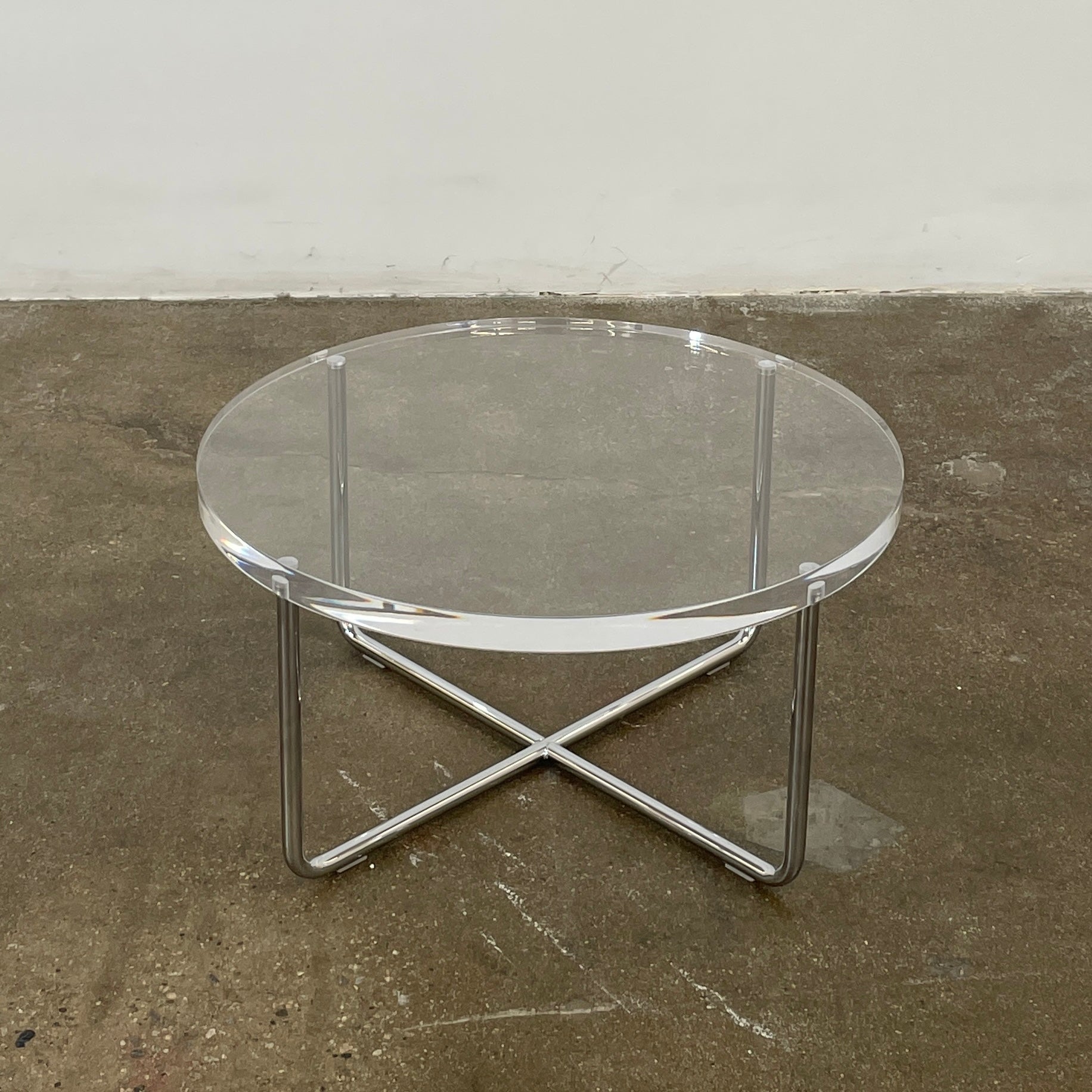 The Minotti Lucite Accent Table boasts a round glass top with a chrome metal frame and crossed base, capturing the Italian elegance synonymous with Minotti's design.